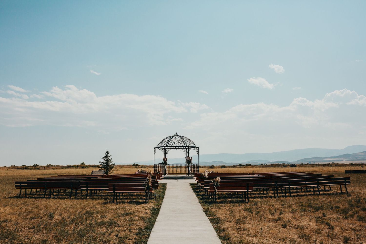 White wooden walkway leads to wedding ceremony arch in rustic outdoor mountain setting.