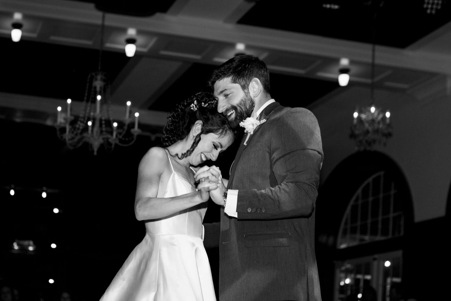 An intimate first dance moment captured in black and white under chandelier lighting.