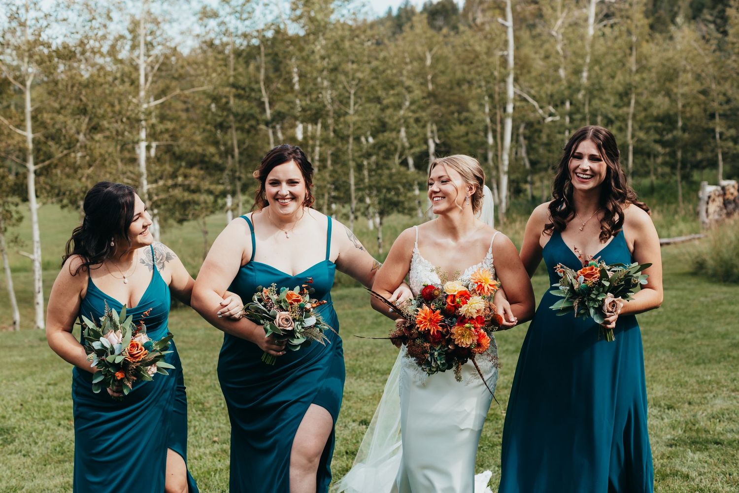 A bridal party in teal dresses holding vibrant orange and yellow bouquets outdoors.