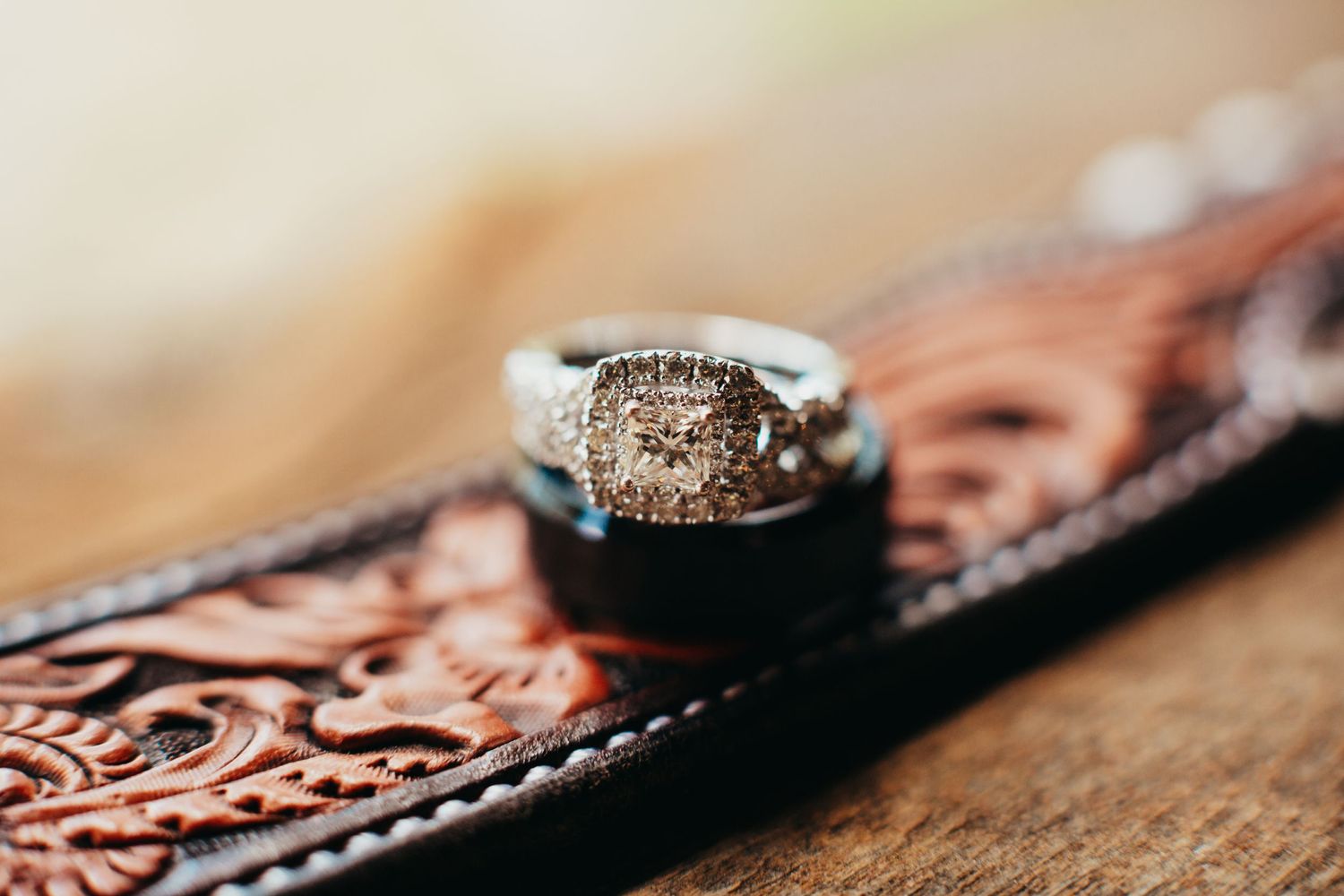 A sparkly diamond engagement ring rests on an ornate leather surface in macro detail.