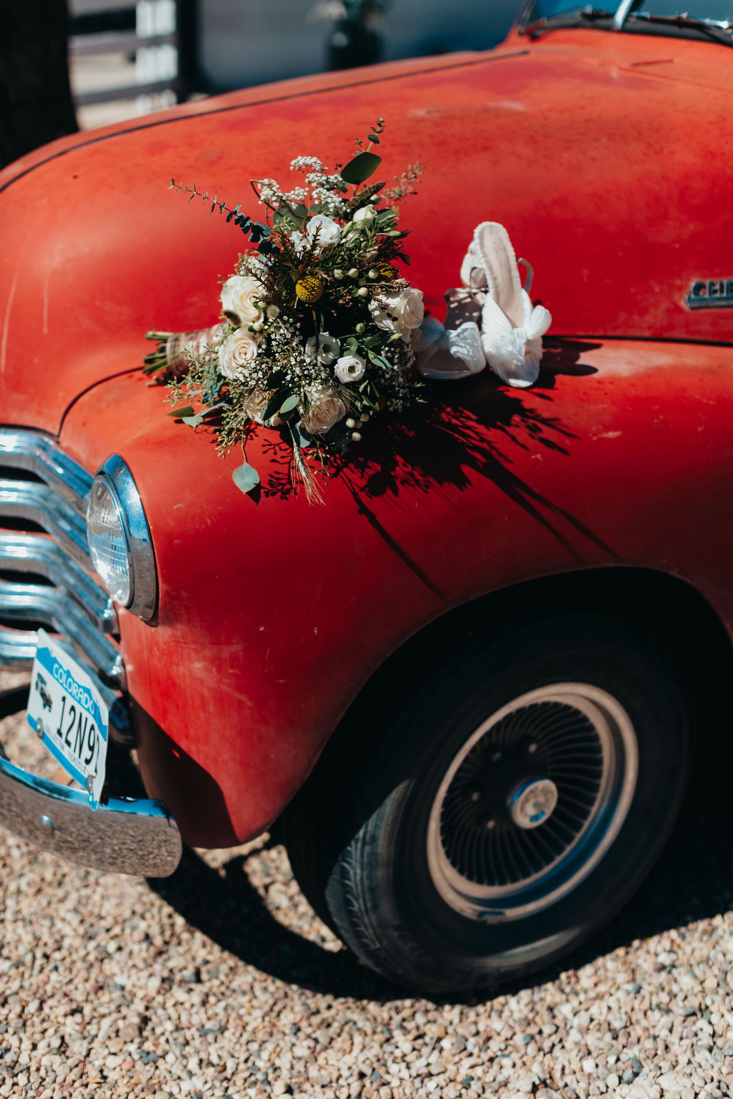 Wedding bouquet rests on hood of vintage red car with chrome details.