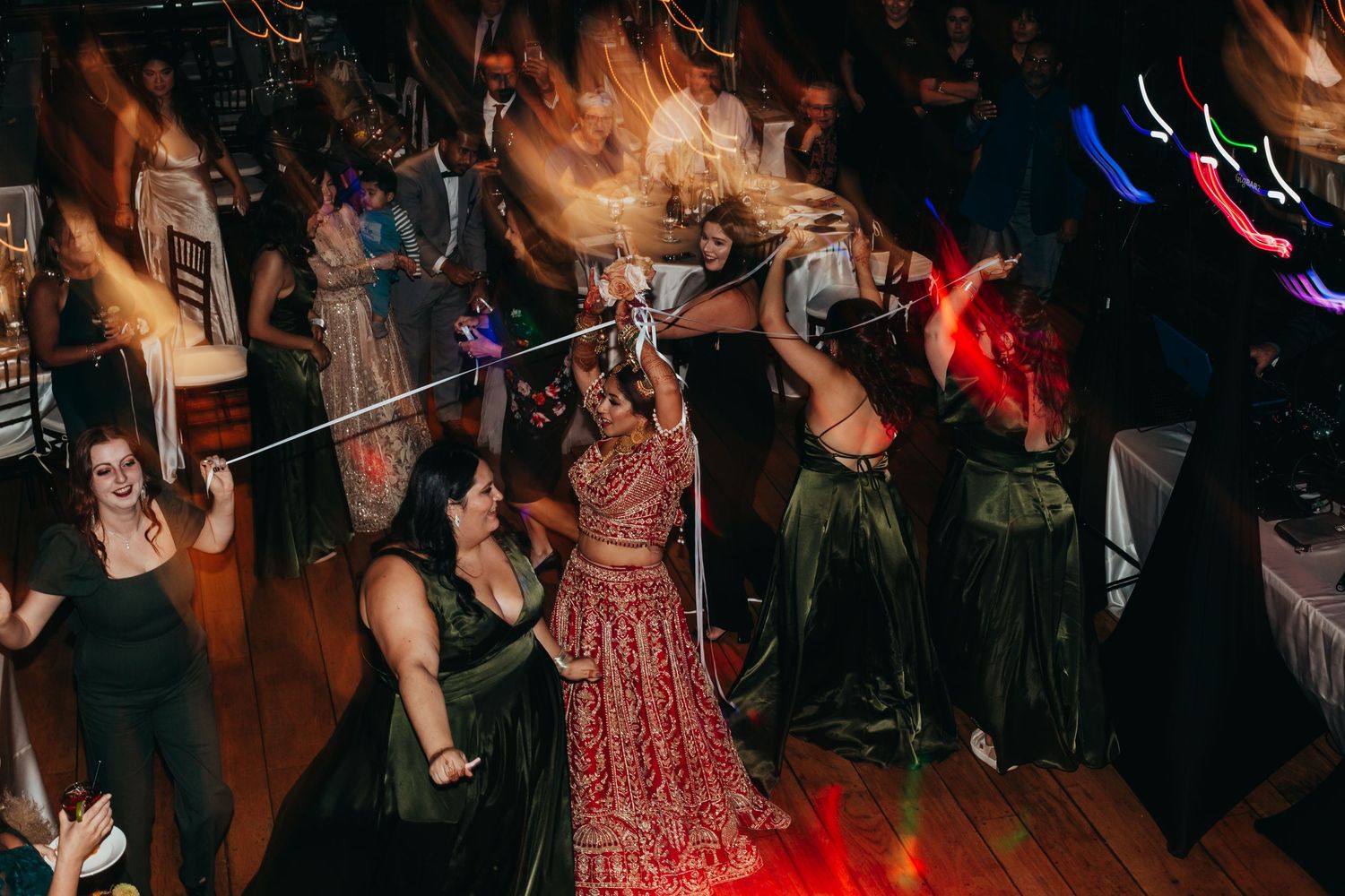 Wedding celebration with dancing guests and someone in a red traditional dress on the dance floor.