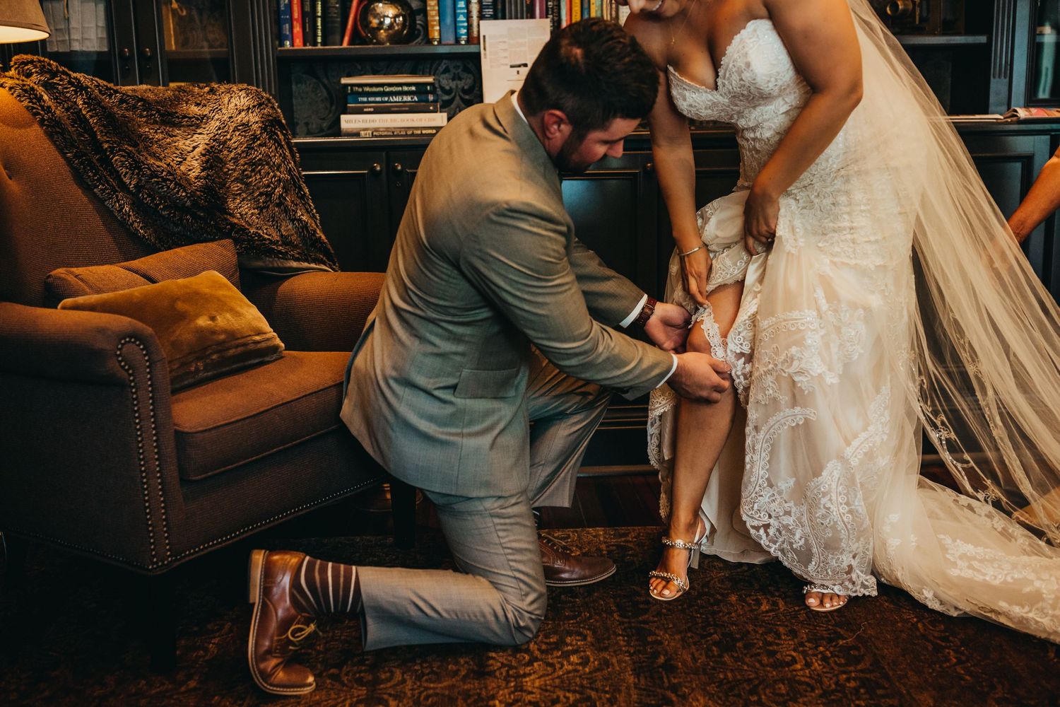 Traditional garter removal moment captured in elegant library setting with vintage furniture.