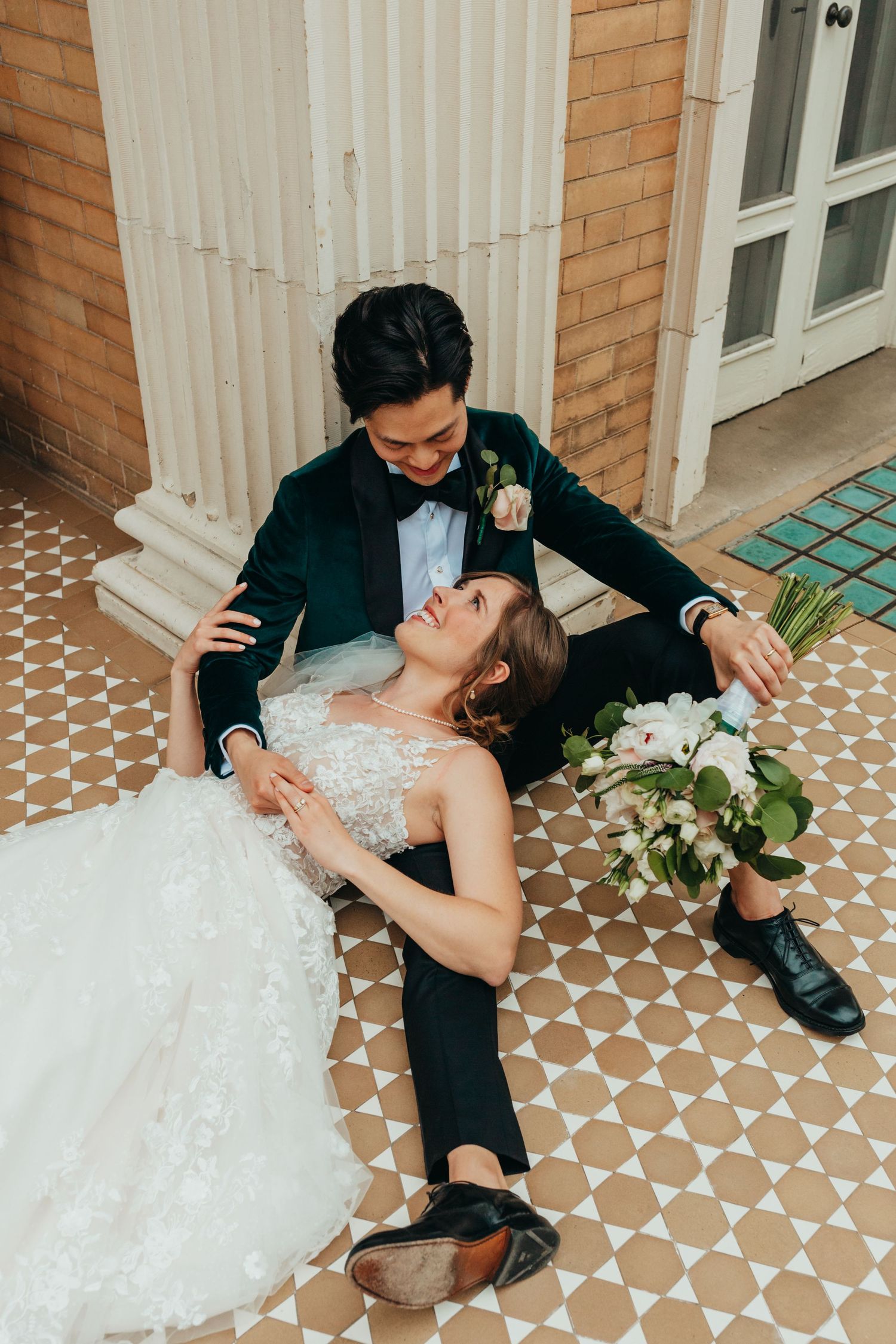 Romantic wedding couple poses on a tiled porch as the bride dips back holding white flowers.