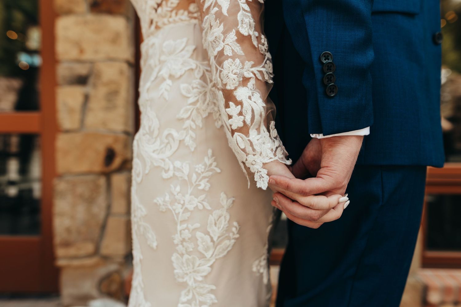 Close-up detail of lace wedding dress and navy suit during an intimate moment.
