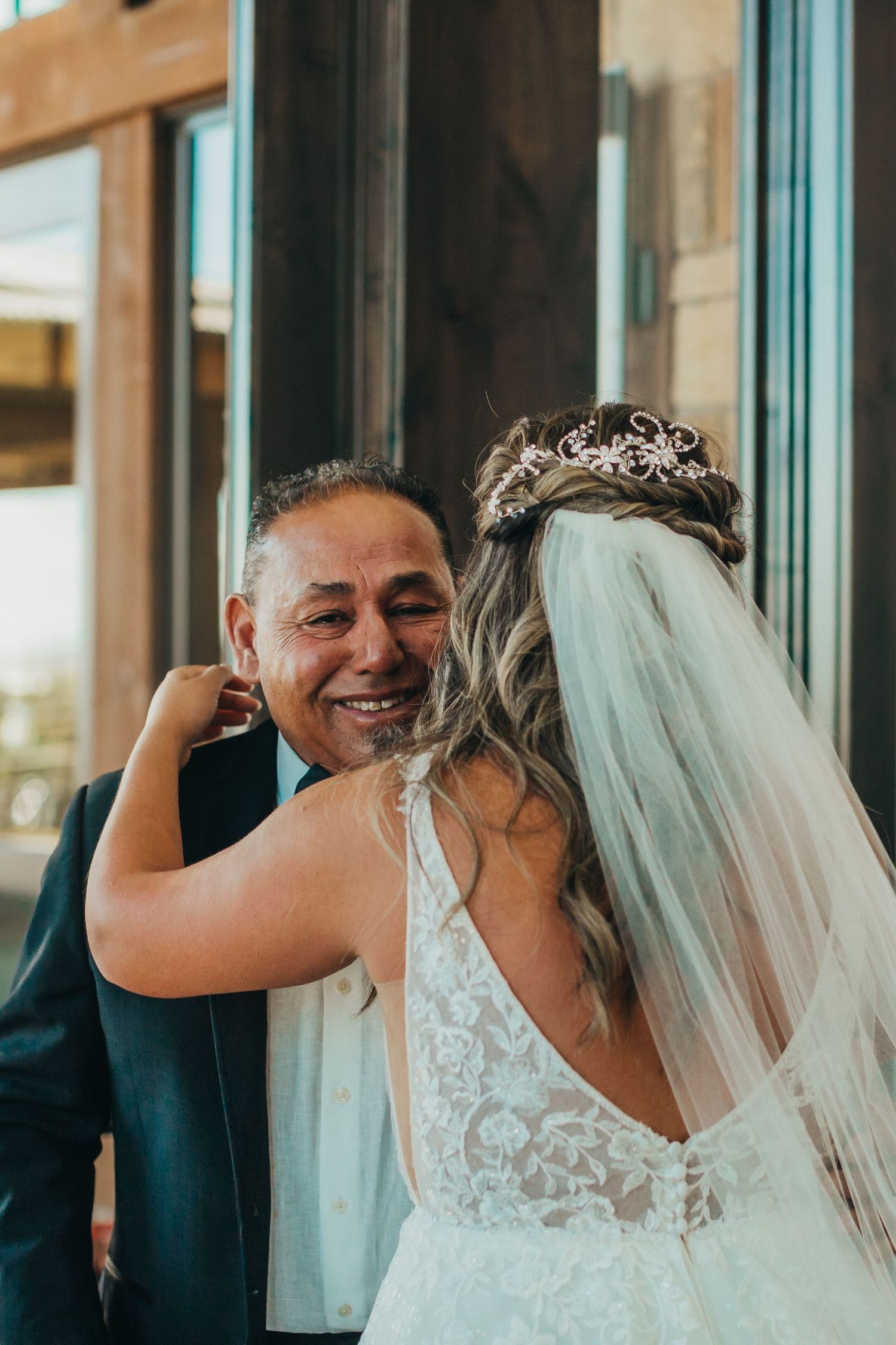 Heartfelt embrace shared between bride in lace gown and wedding guest during celebration.