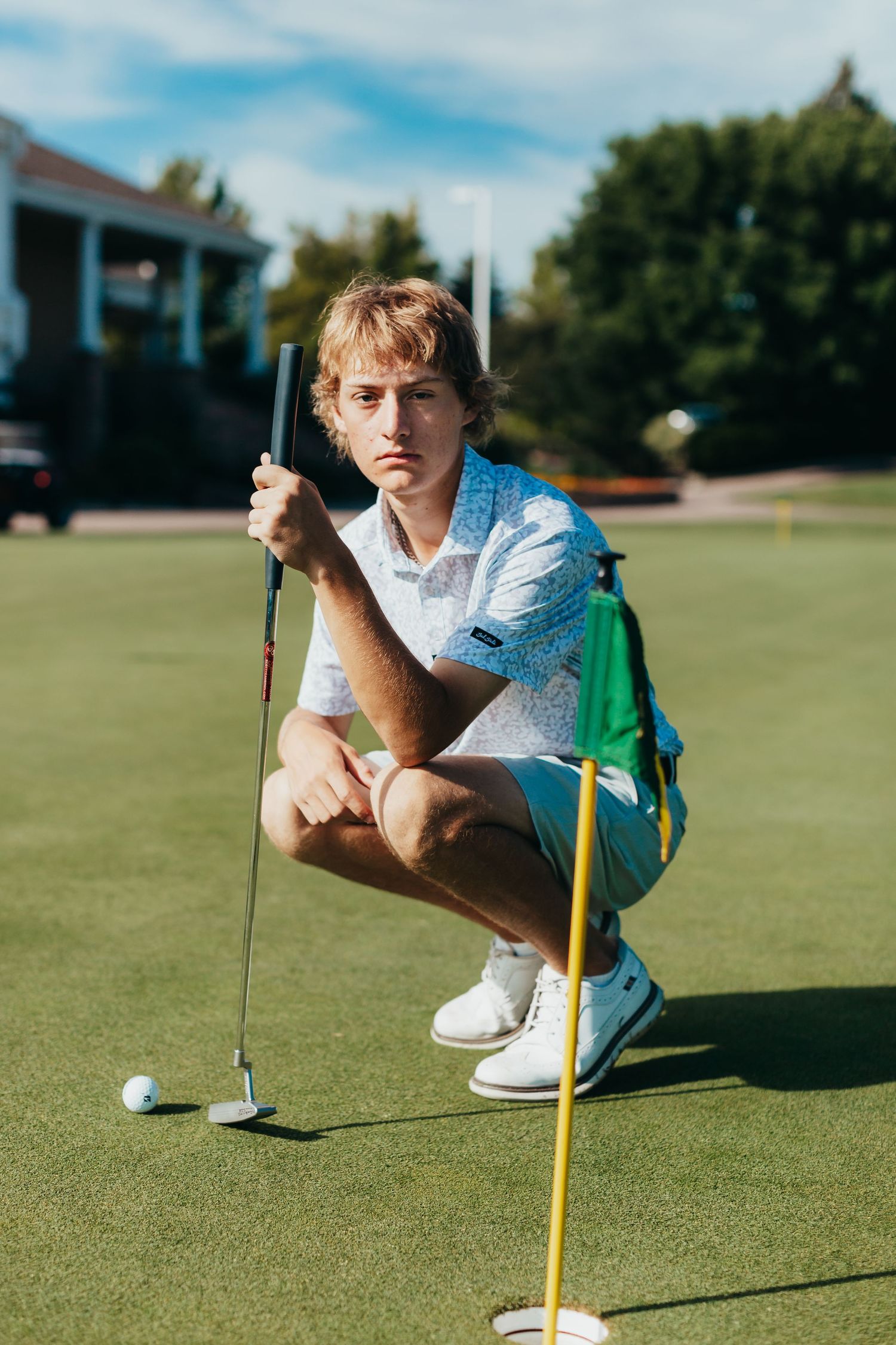A golfer crouches on the green to line up a putt on a sunny day.