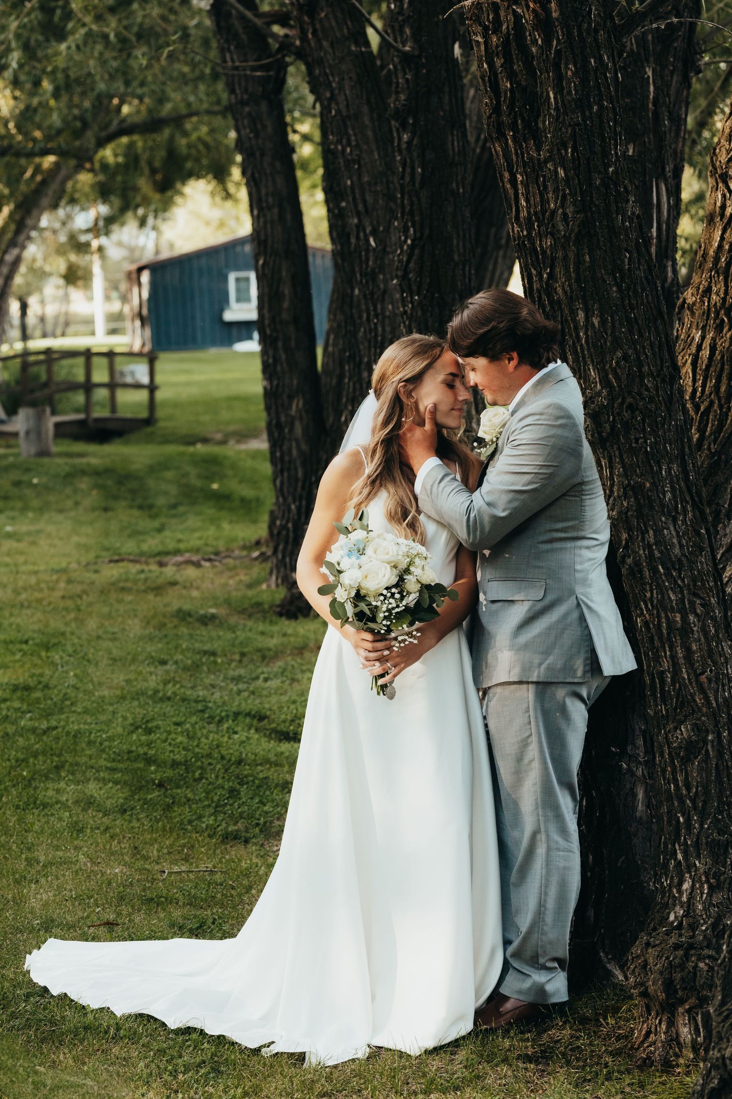 Romantic couple shares intimate moment against large tree trunk during outdoor wedding.