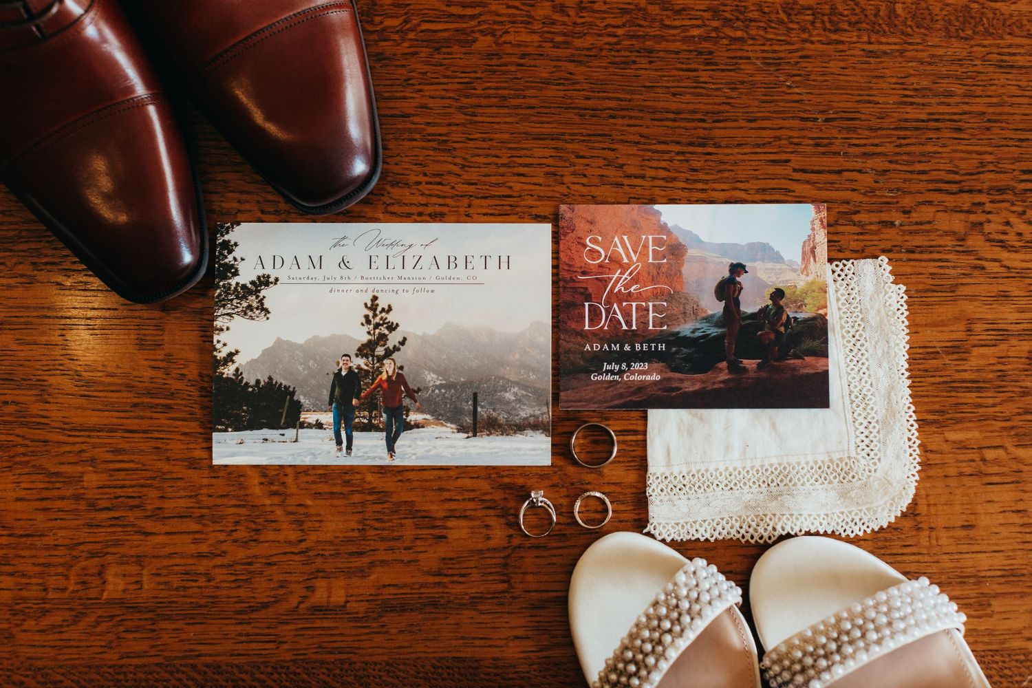 Wedding details flatlay with save the date cards, brown leather shoes, and rings on wooden surface.