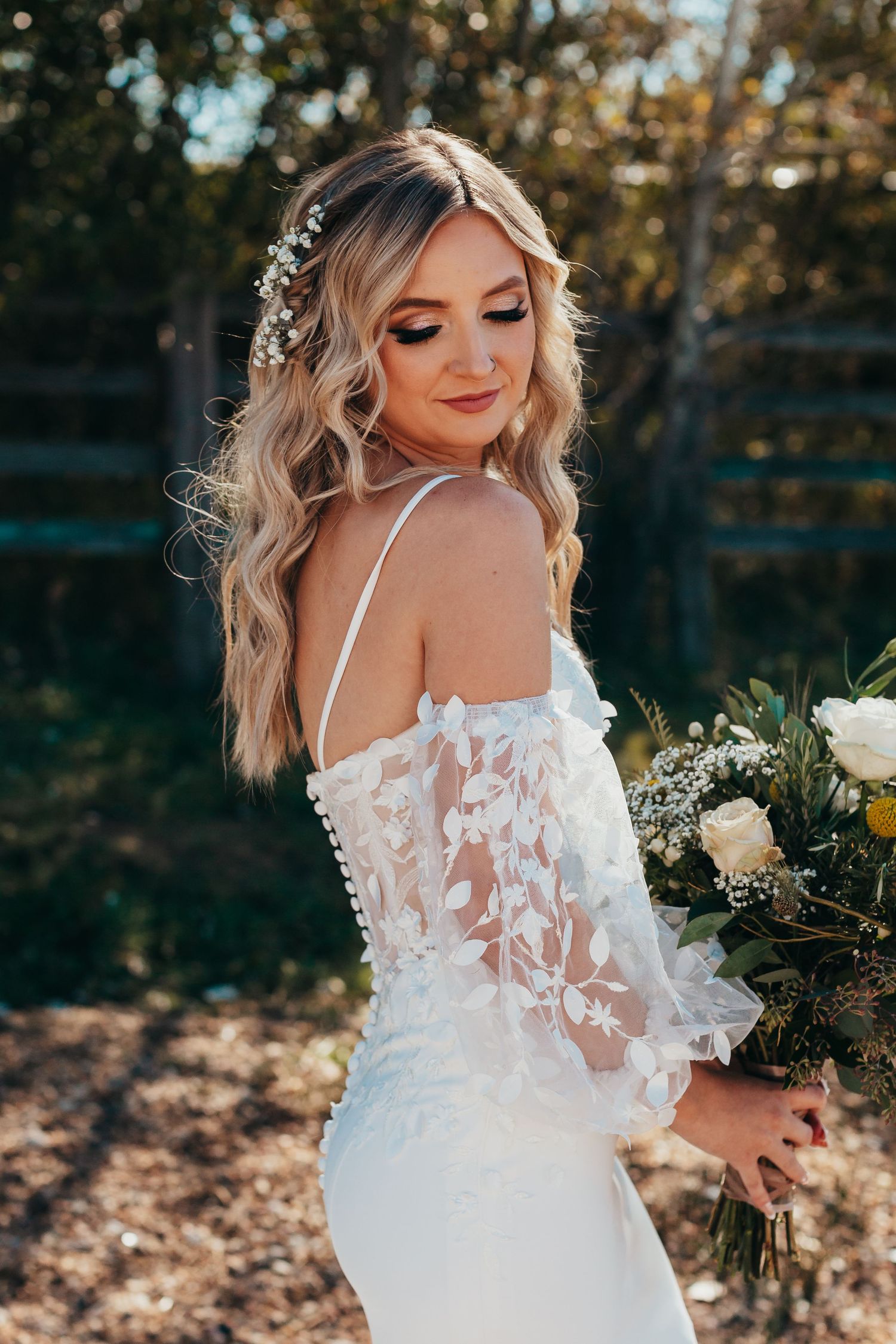 Elegant wedding dress with delicate lace sleeves and floral hair accessories in an outdoor setting.