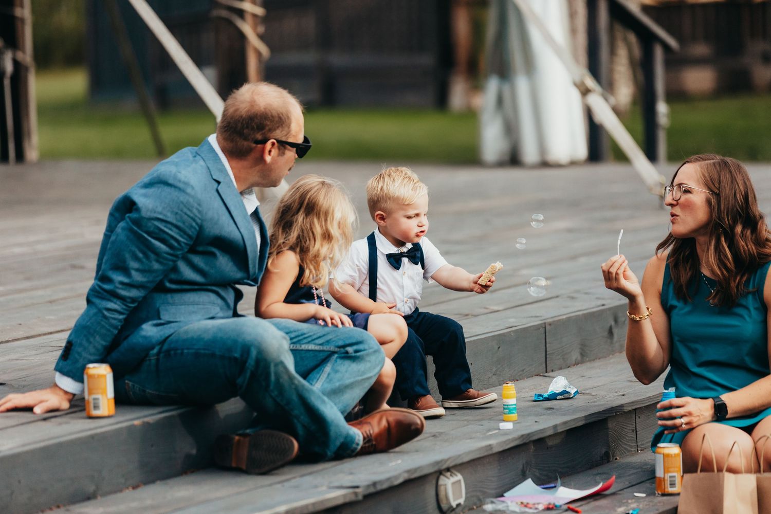Family enjoys casual moment sitting on wooden steps during wedding reception.