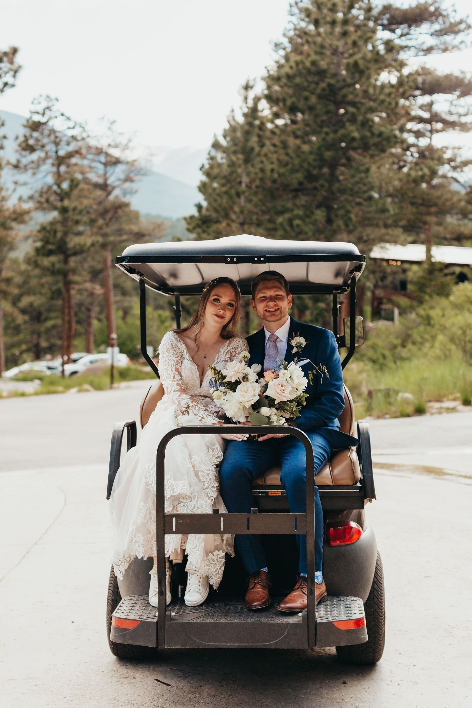 A couple rides in a golf cart through a mountain resort setting.