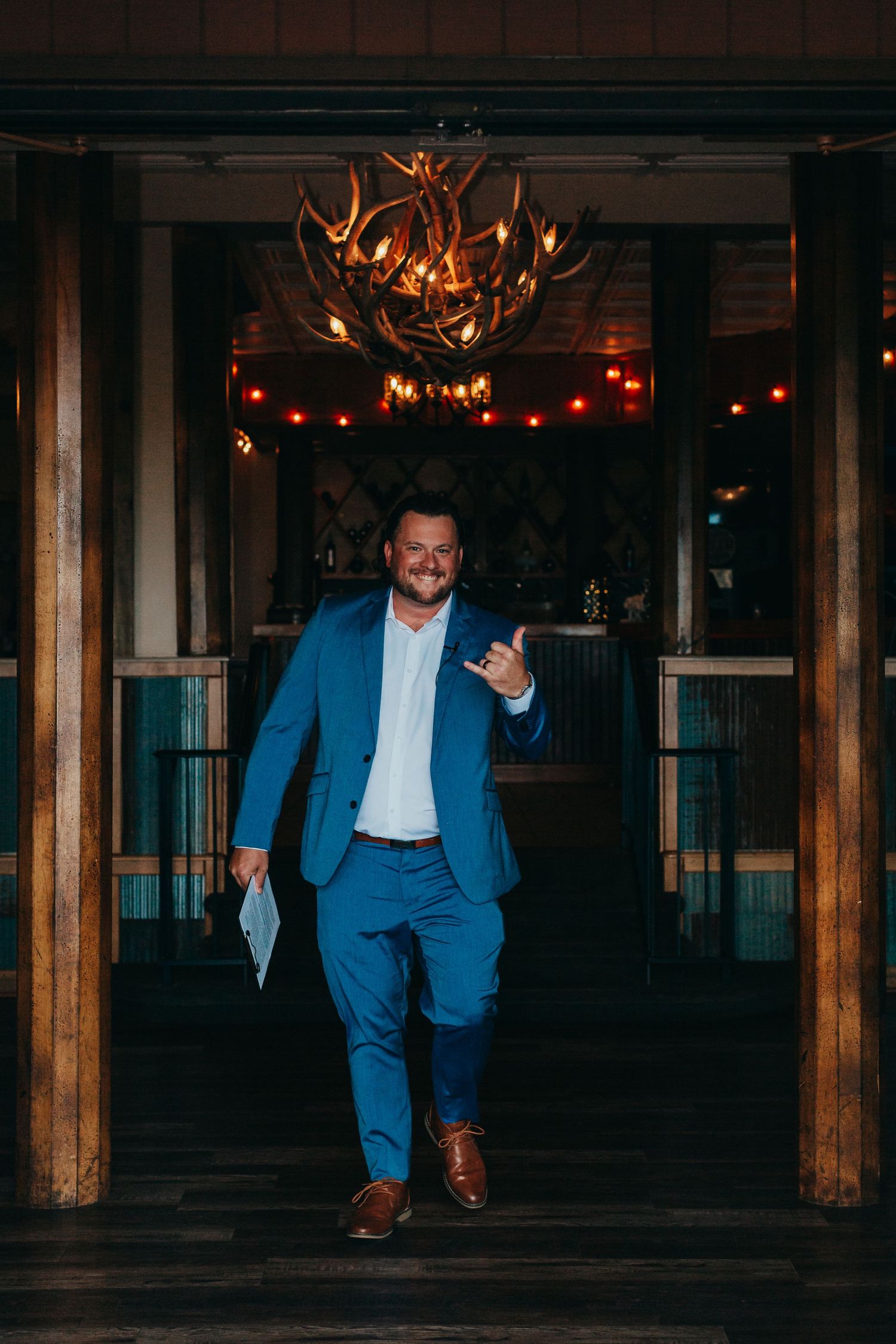 Person in blue suit walking under antler chandelier in rustic venue setting.