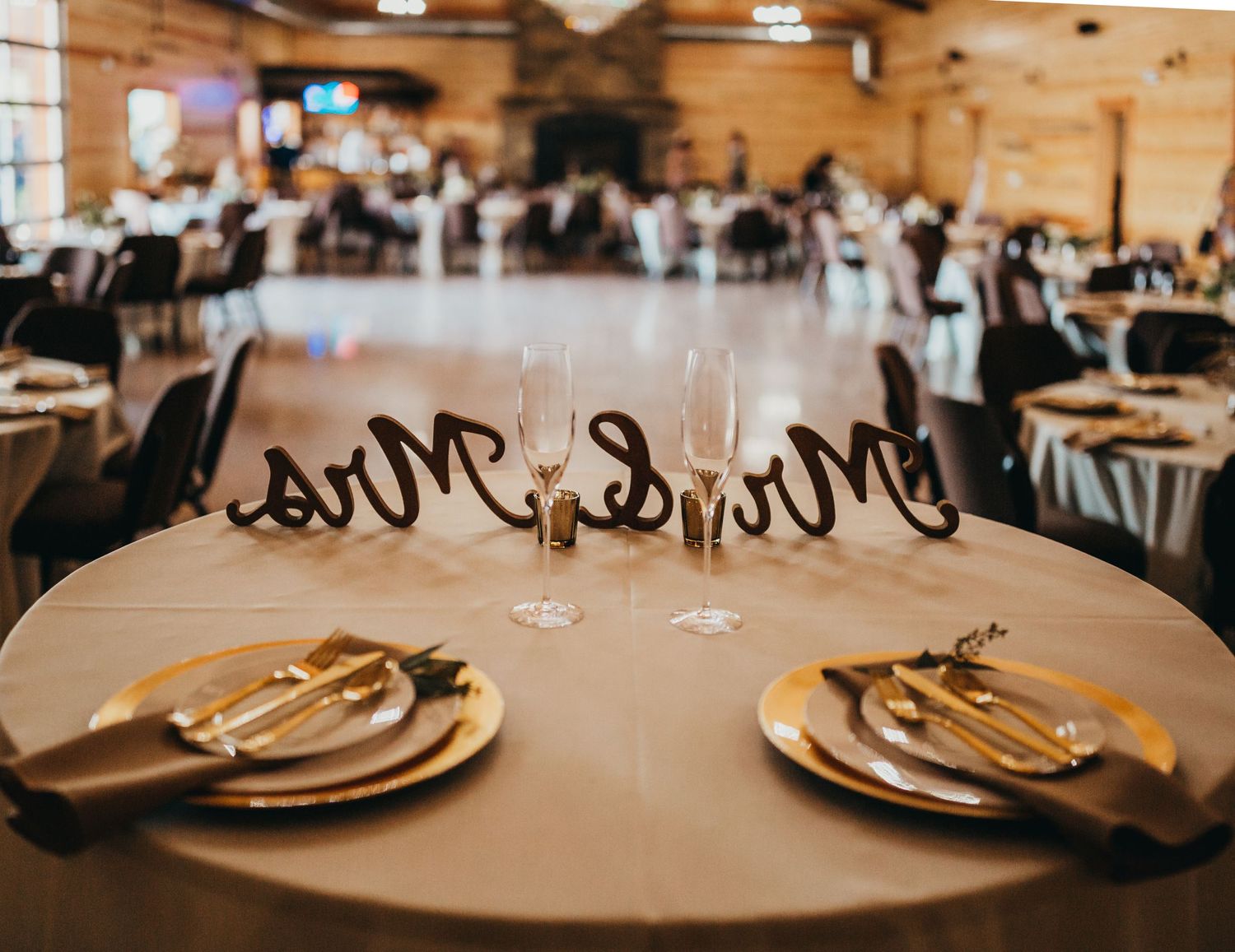 Mr and Mrs table setting with gold plates and rustic decor at wedding reception.