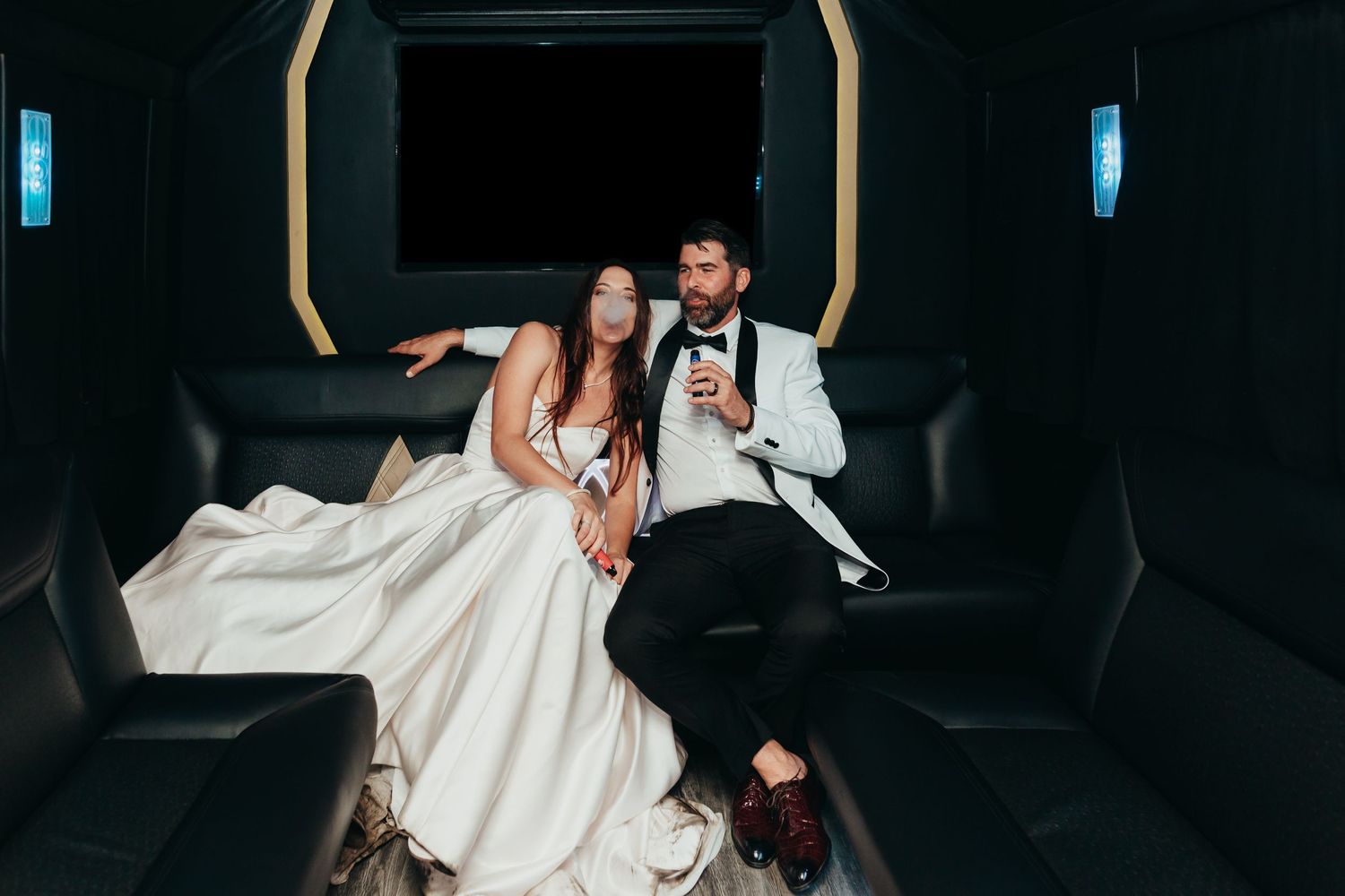 Couple celebrates in back of luxury limousine after wedding ceremony.