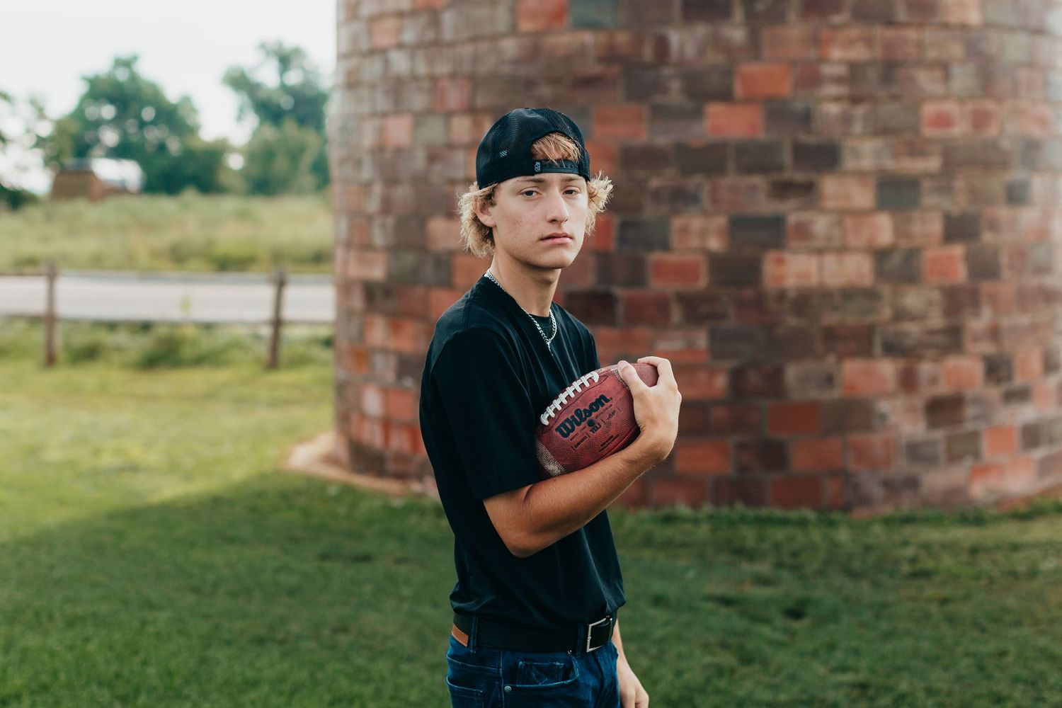 Person in casual attire holding football in front of brick silo structure.