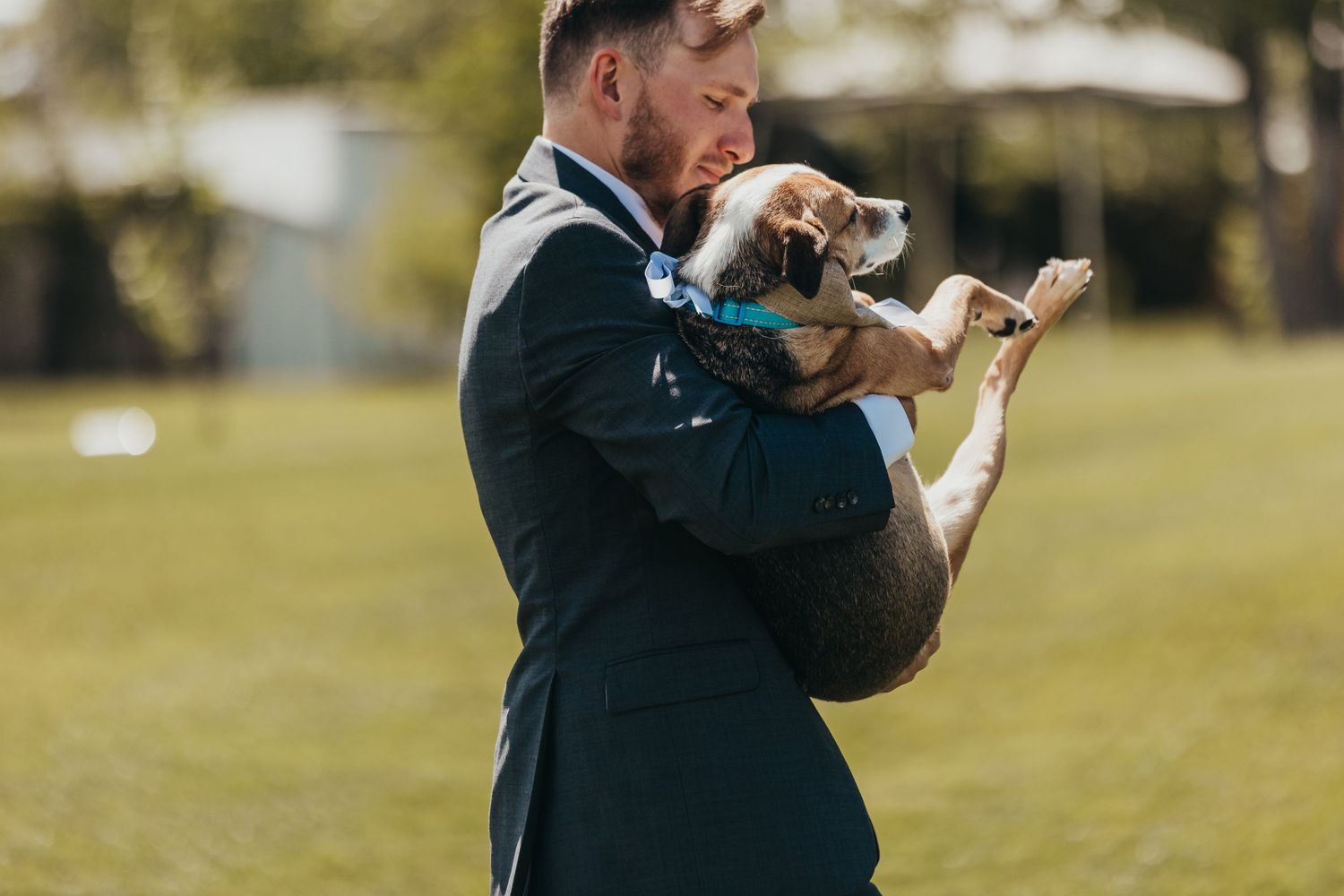 Groom in formal suit holds small cat during outdoor wedding photoshoot.