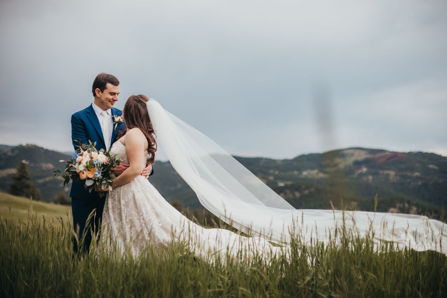 Wedding couple embracing on a hillside with dramatic mountain landscape behind them.