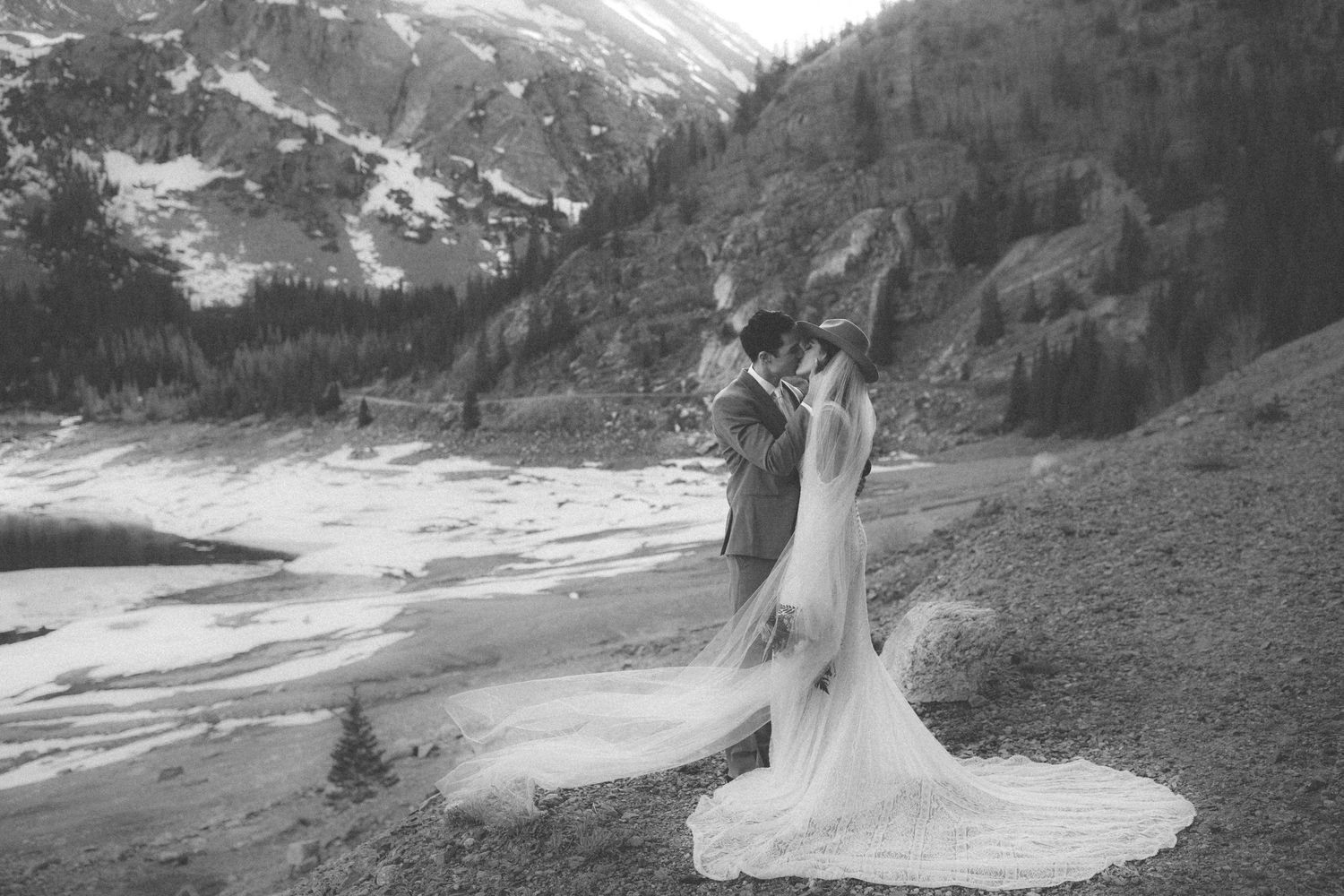 A black and white wedding photo with dramatic mountain scenery and flowing dress train.