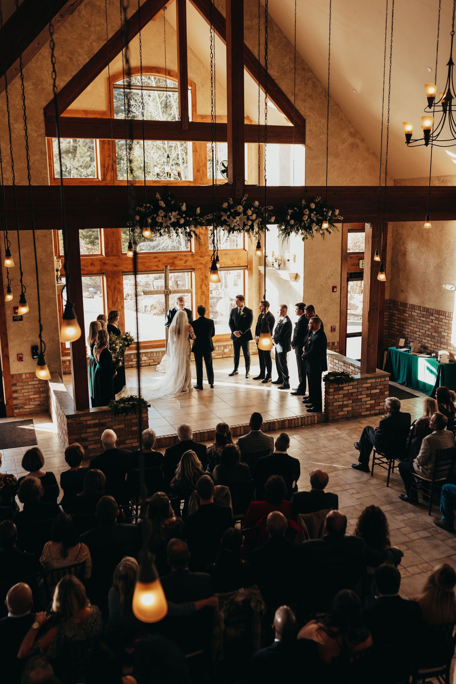 Indoor wedding ceremony in rustic venue with exposed beams and dramatic lighting.