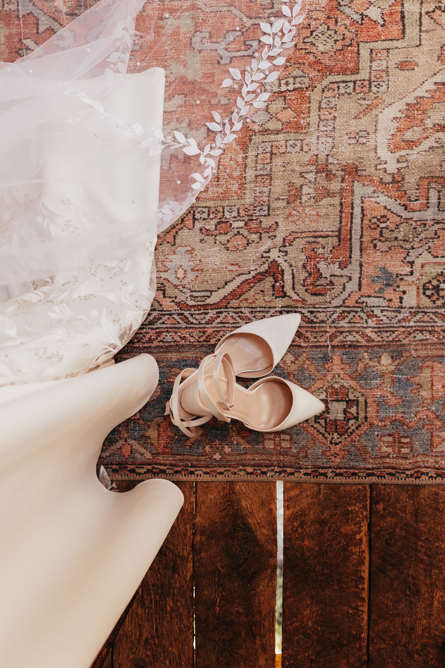 White wedding shoes and veil placed on a vintage patterned carpet.