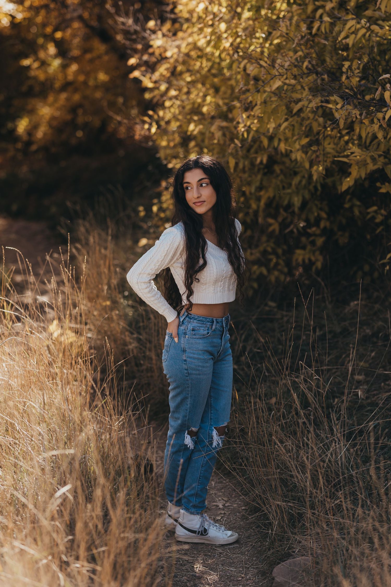 Casual portrait of woman in crop top and jeans against autumn foliage.