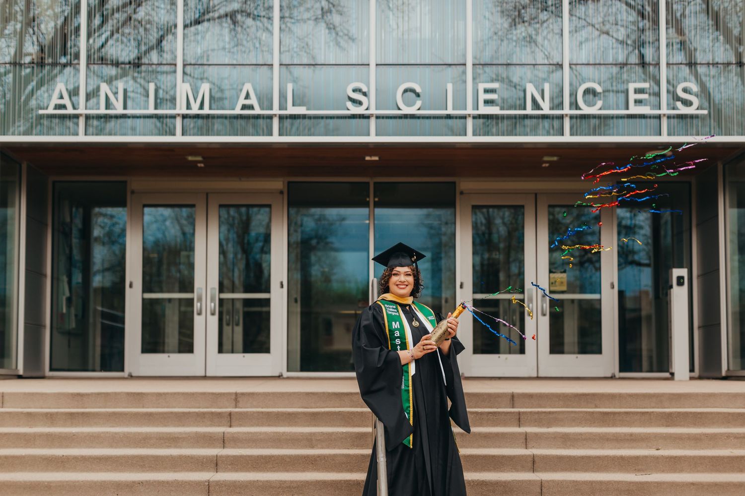Graduate in cap and gown poses in front of Animal Sciences building.