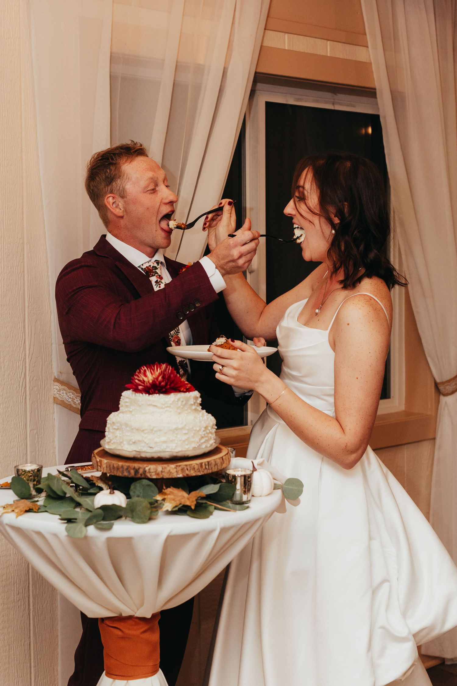 A couple playfully feeding each other wedding cake at their reception.