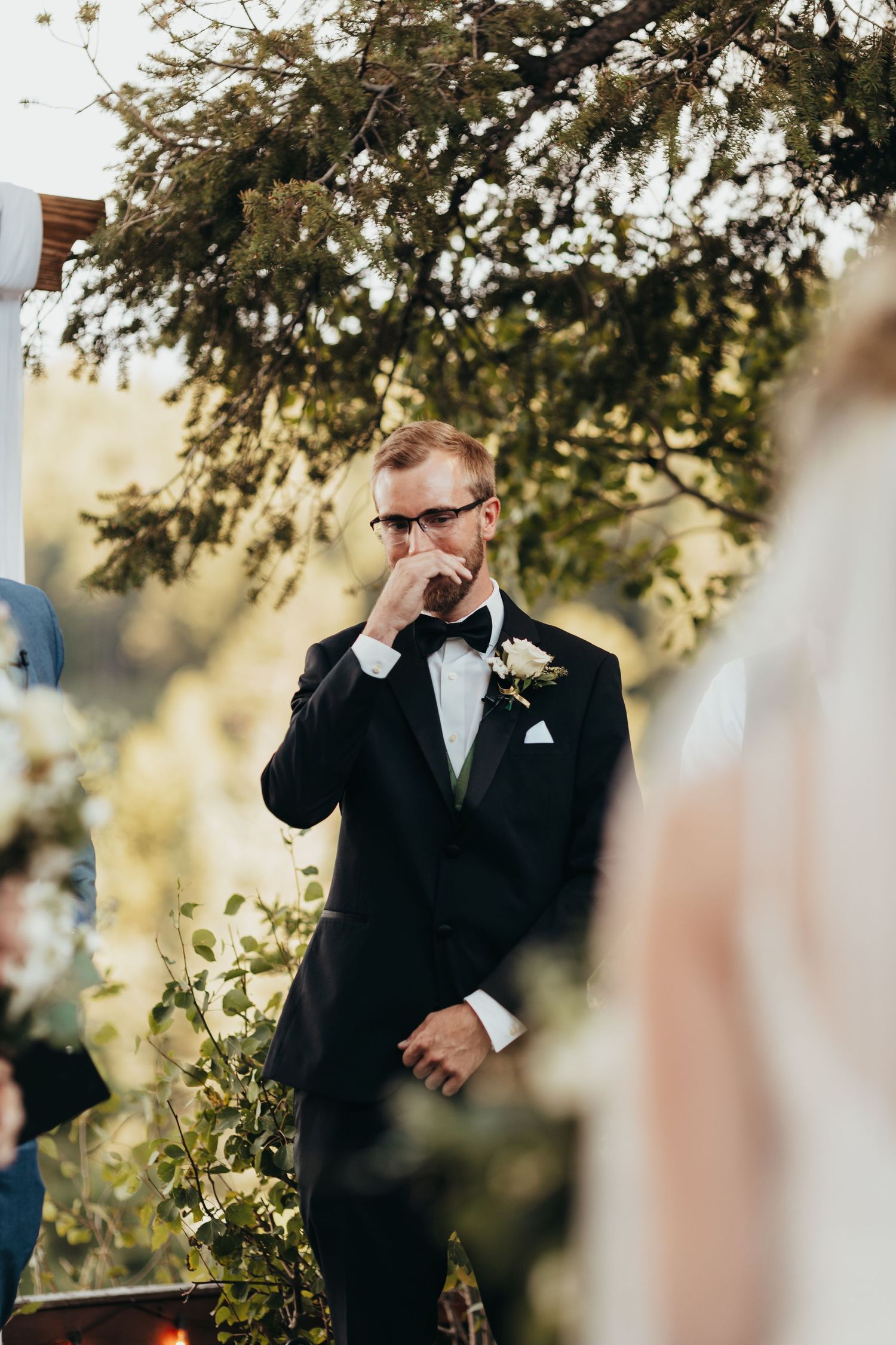 Emotional wedding ceremony moment captured outdoors with natural sunlight filtering through trees.