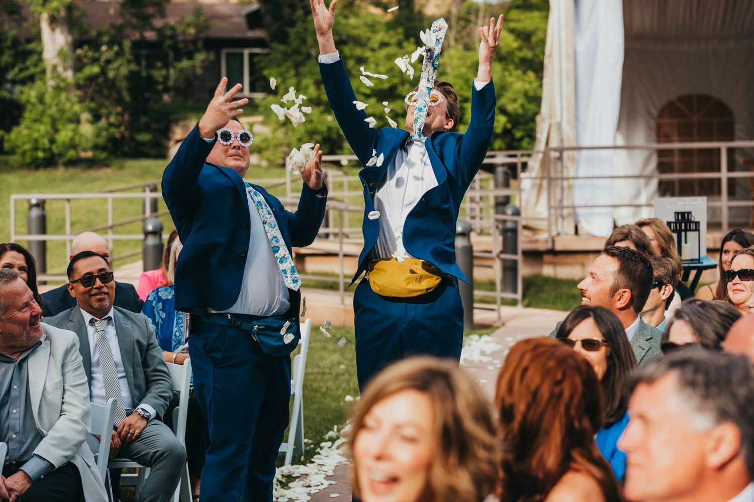 Wedding guests celebrate with raised arms during outdoor ceremony.