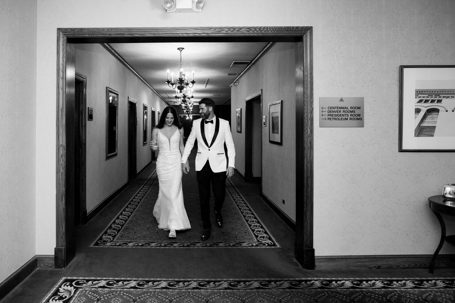 Black and white photo of couple walking down elegant hotel hallway.