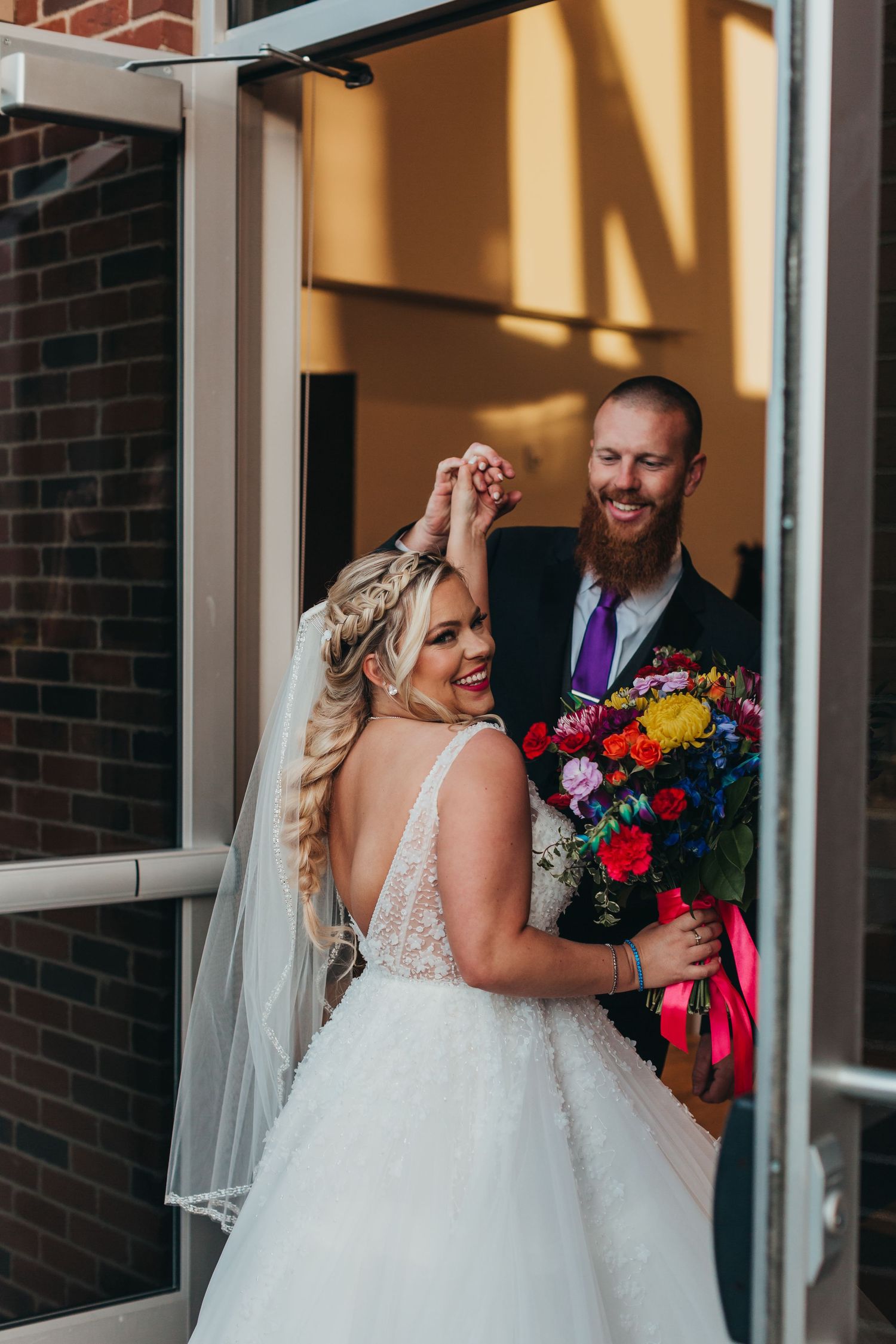 Joyful wedding moment captured in a doorway with a vibrant floral bouquet.