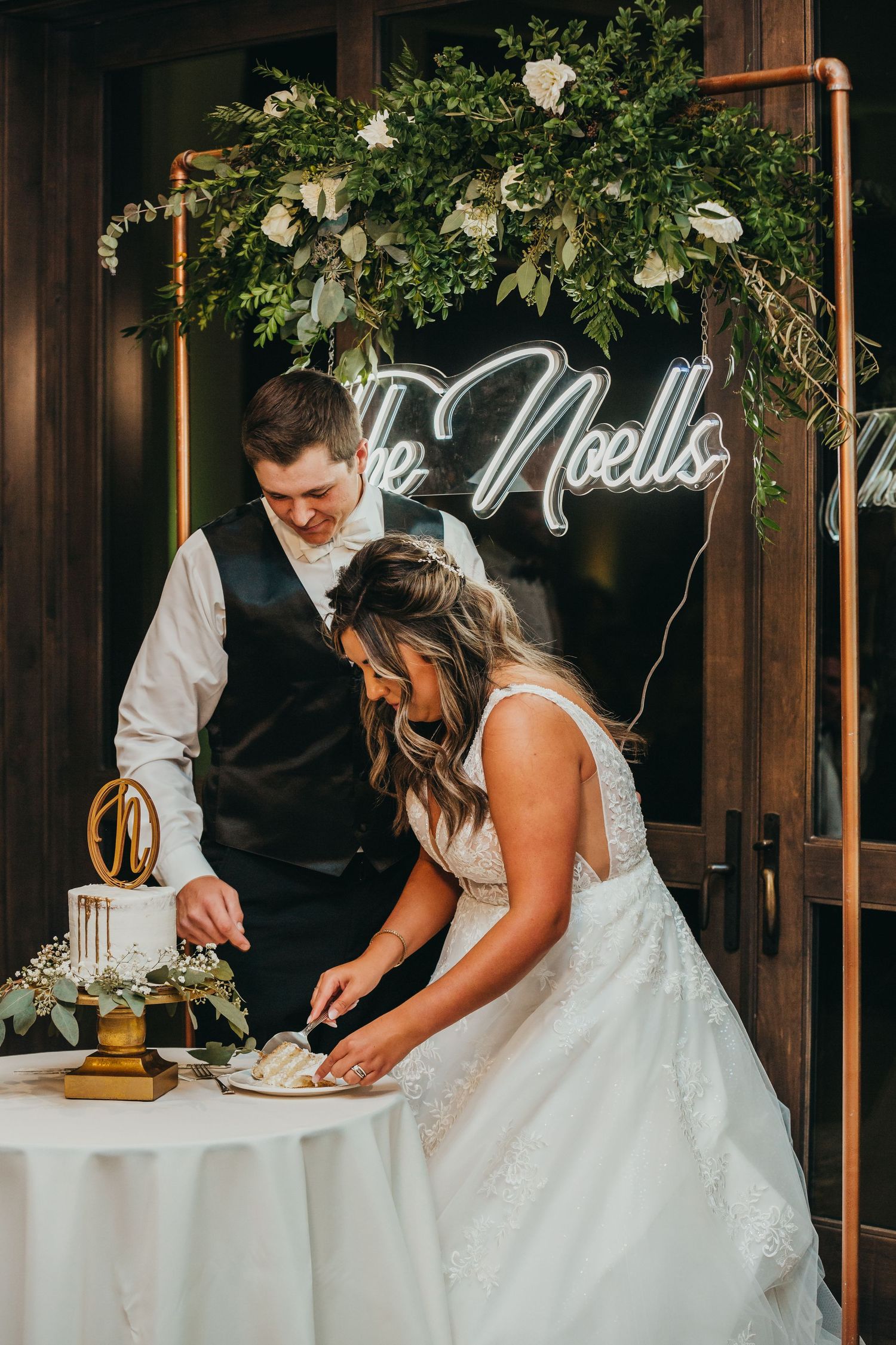 Couple cutting their wedding cake beneath a floral arch with neon signage.