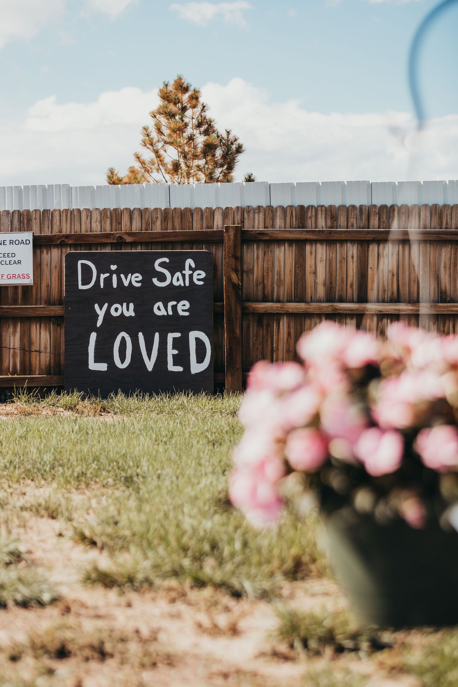 A wooden fence displays a heartfelt chalk message reading 'Drive Safe you are LOVED'.