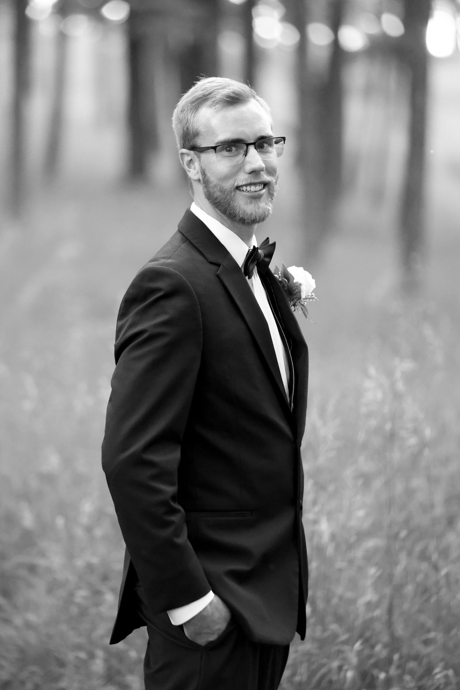Classic black and white portrait of groom in tuxedo with boutonniere standing in field.