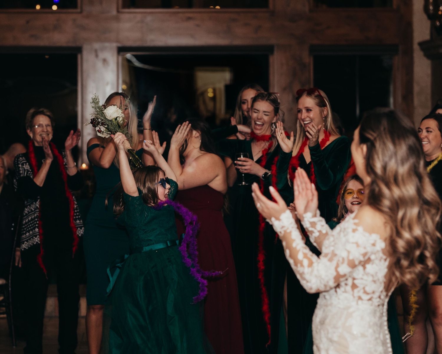 Wedding reception guests celebrate on dance floor in dimly lit venue.