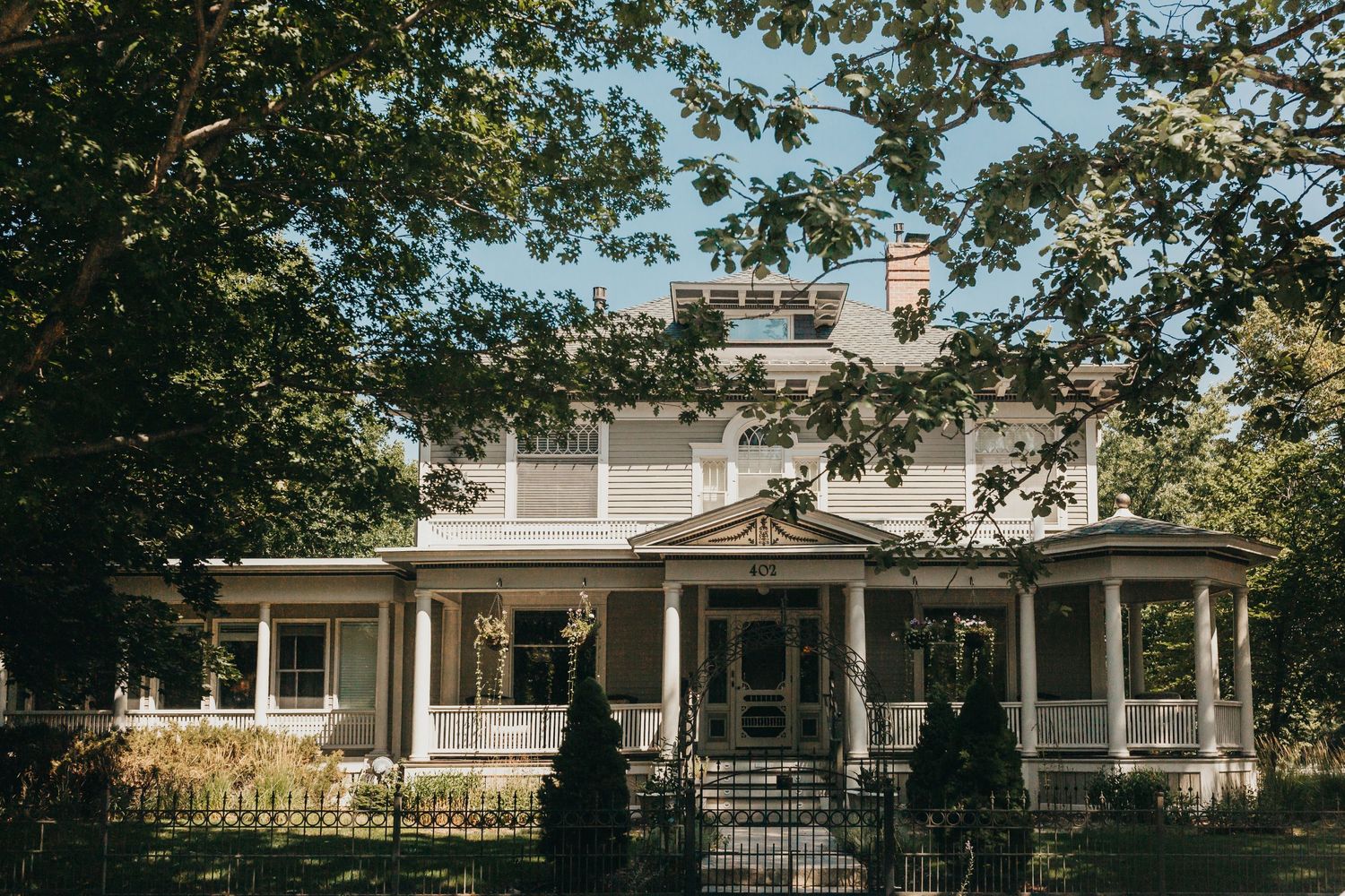 A classic white Victorian-style house with wrap-around porch and landscaped front yard on a sunny day.