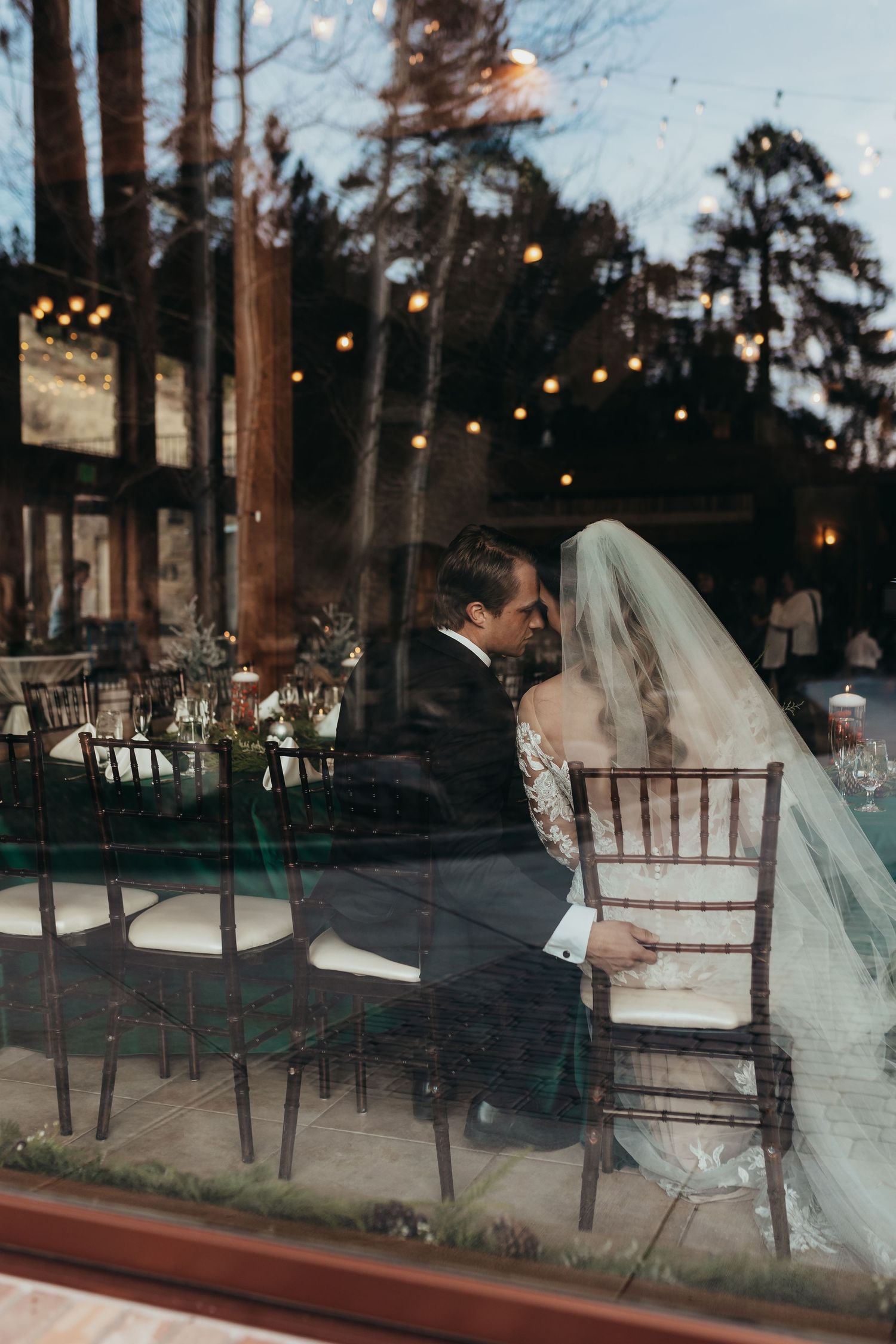 Reception venue with string lights reflecting in window as couple shares intimate moment.
