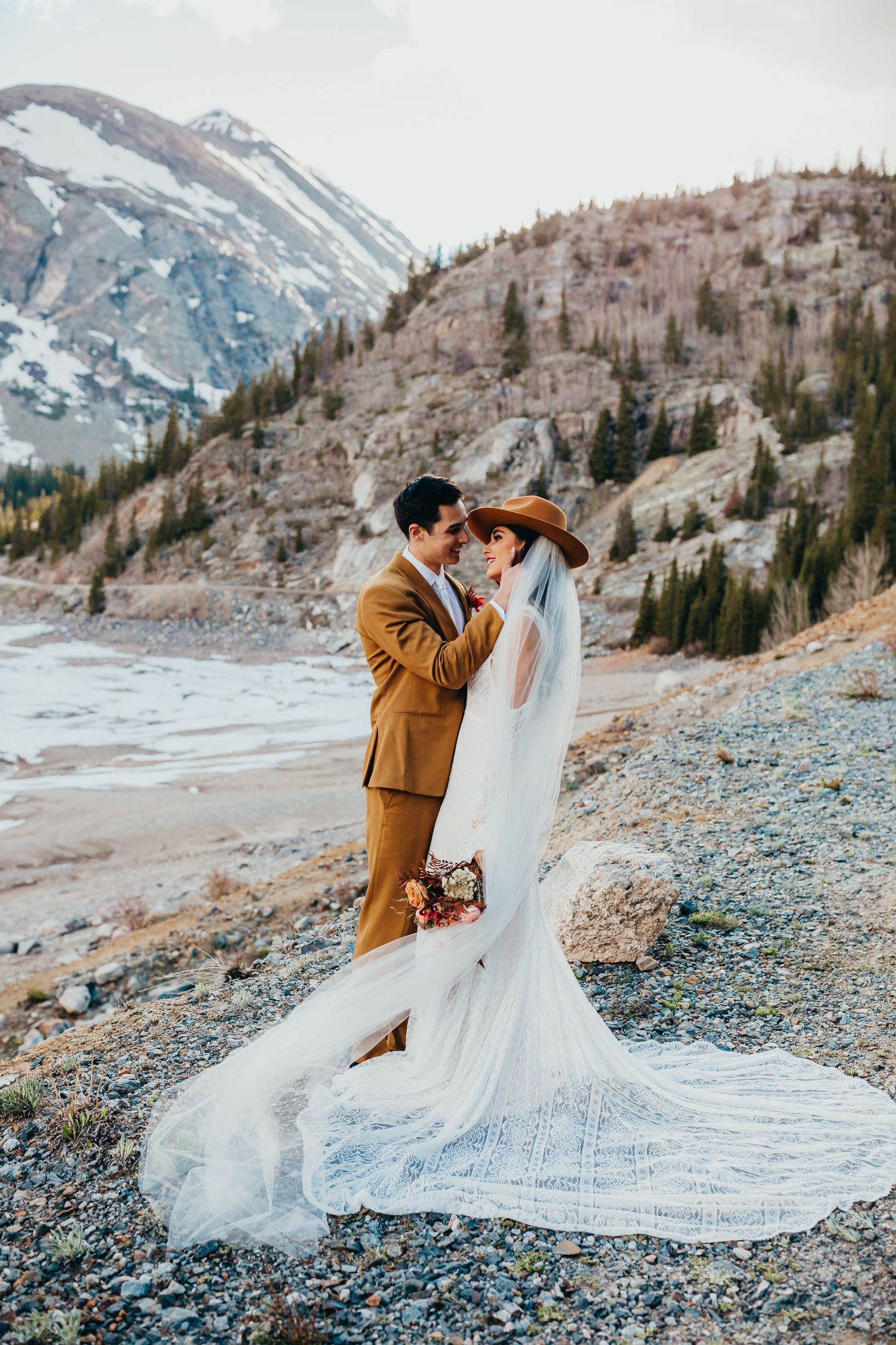 A dramatic wedding photo showing a flowing train dress against mountainous winter landscape.