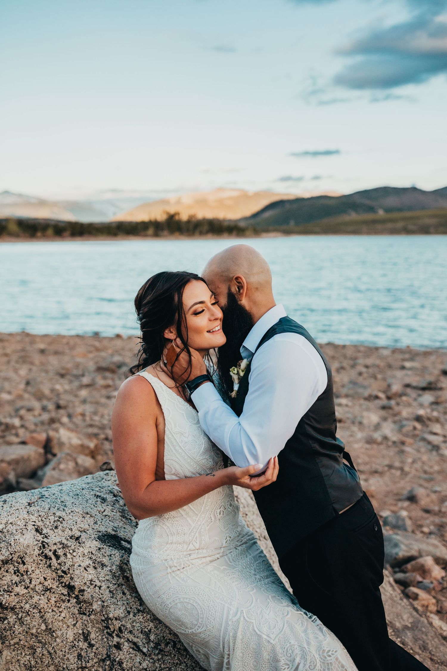 Intimate wedding portrait by mountain lake at golden hour.