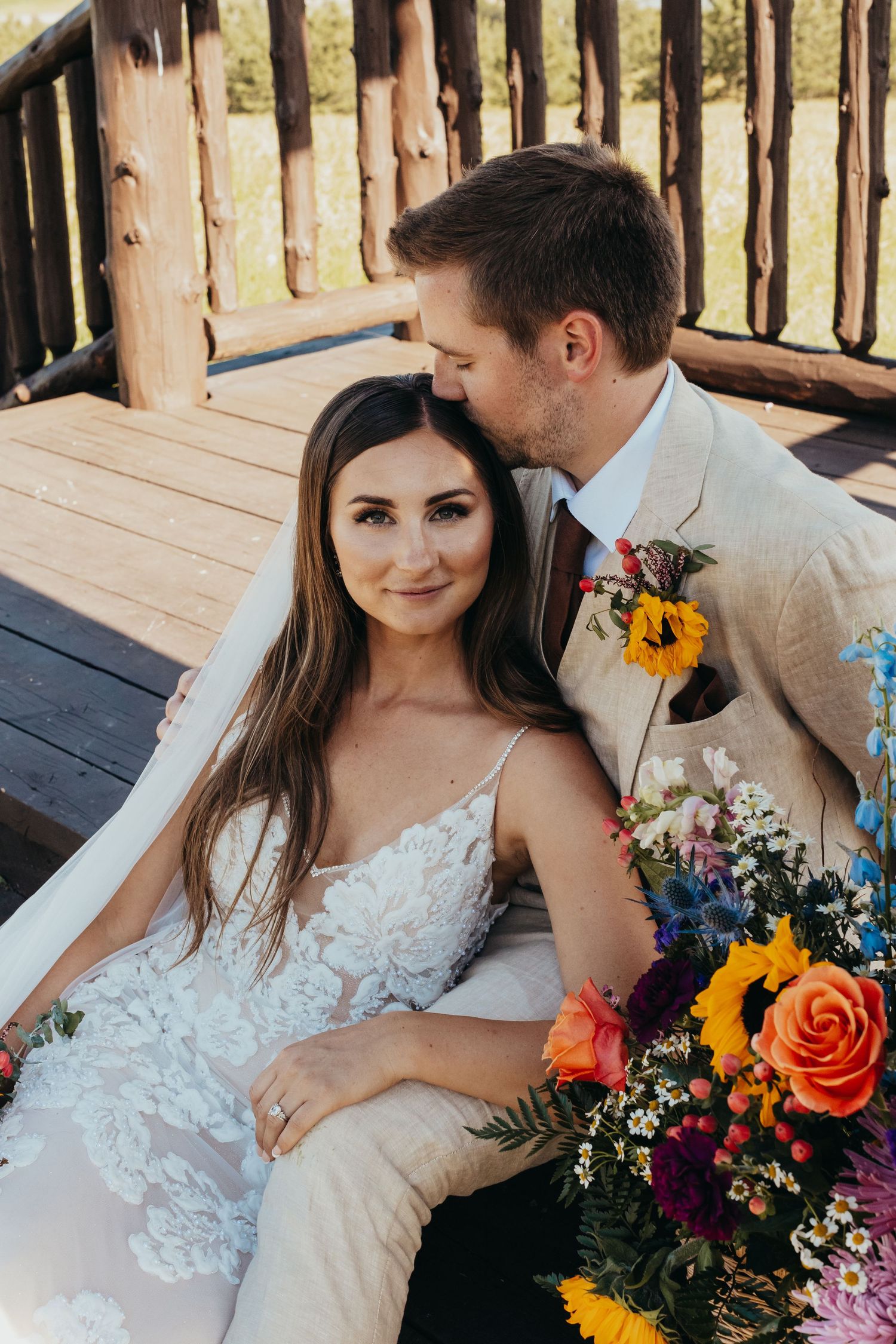 Couple shares tender moment on rustic deck with colorful wildflower bouquet.