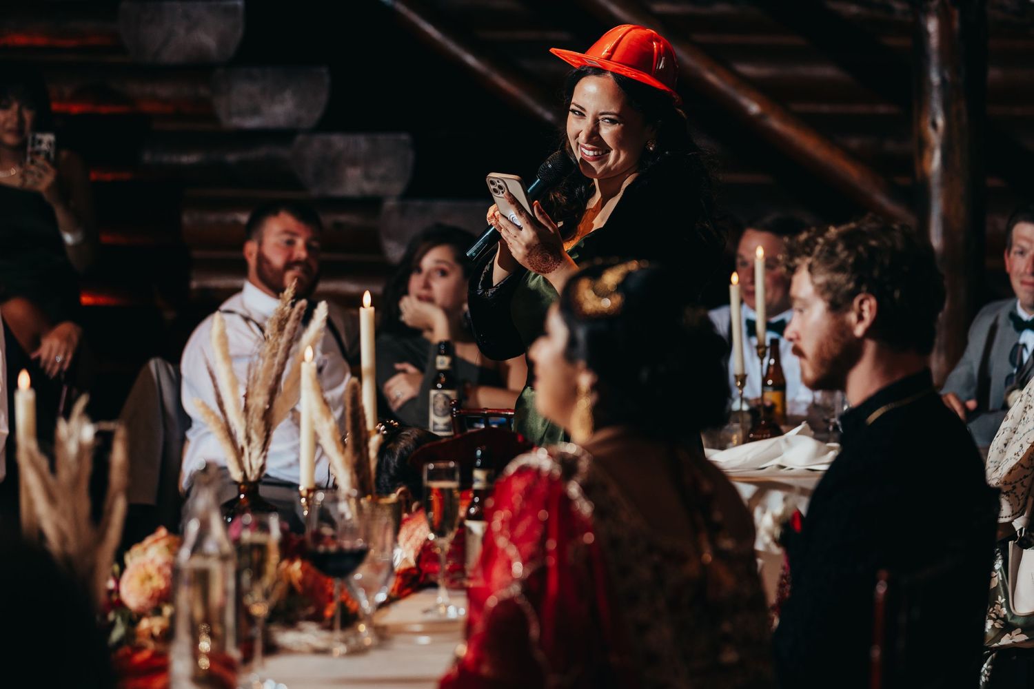 Guests celebrate at a lively wedding reception with a person in red cap holding a microphone.