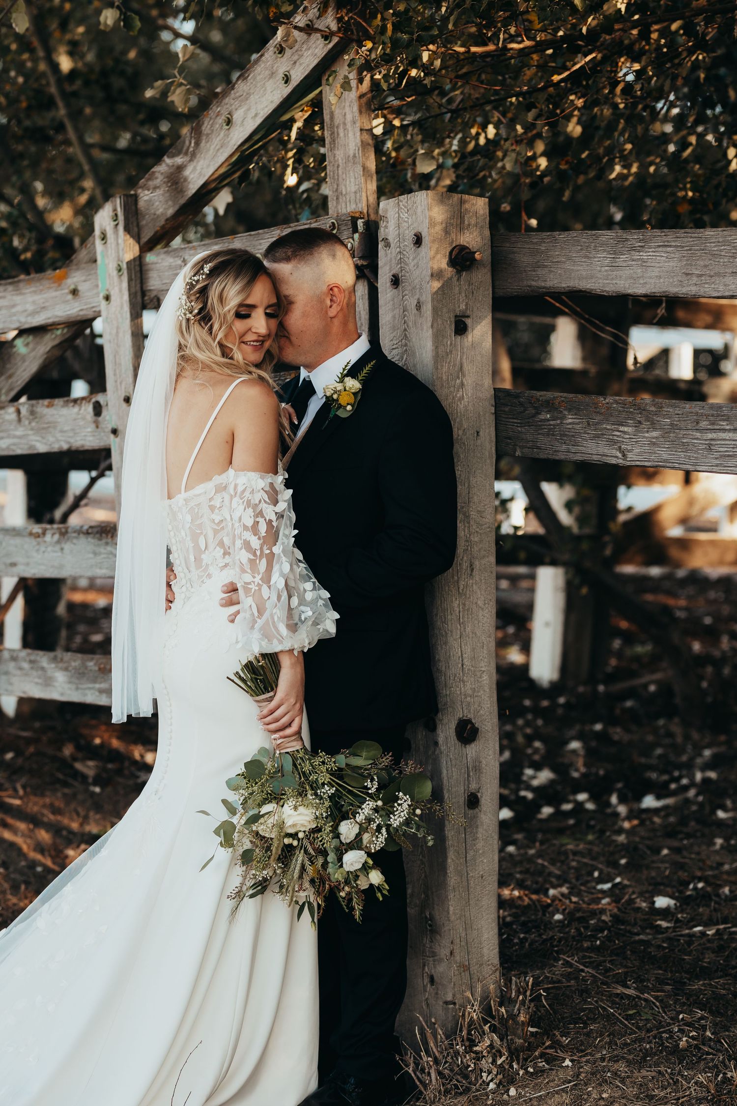 An intimate wedding portrait showing couple embracing by a rustic wooden fence.