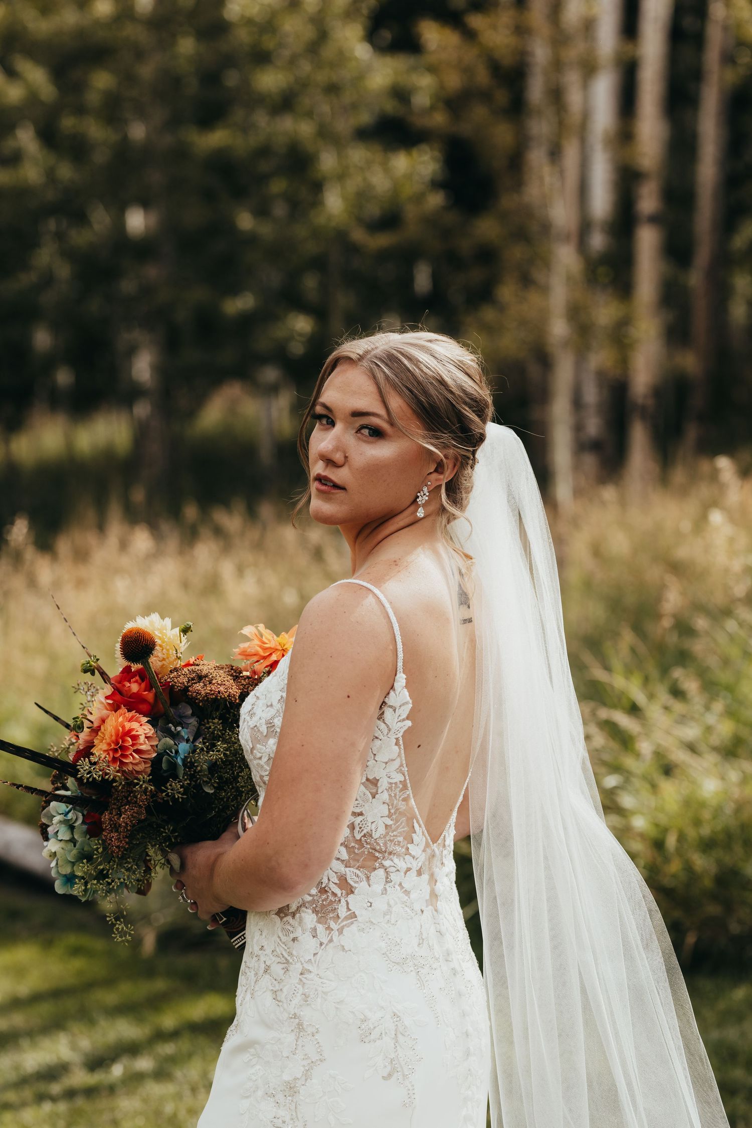A bride in a lace wedding dress holds an autumn bouquet against an aspen grove backdrop.