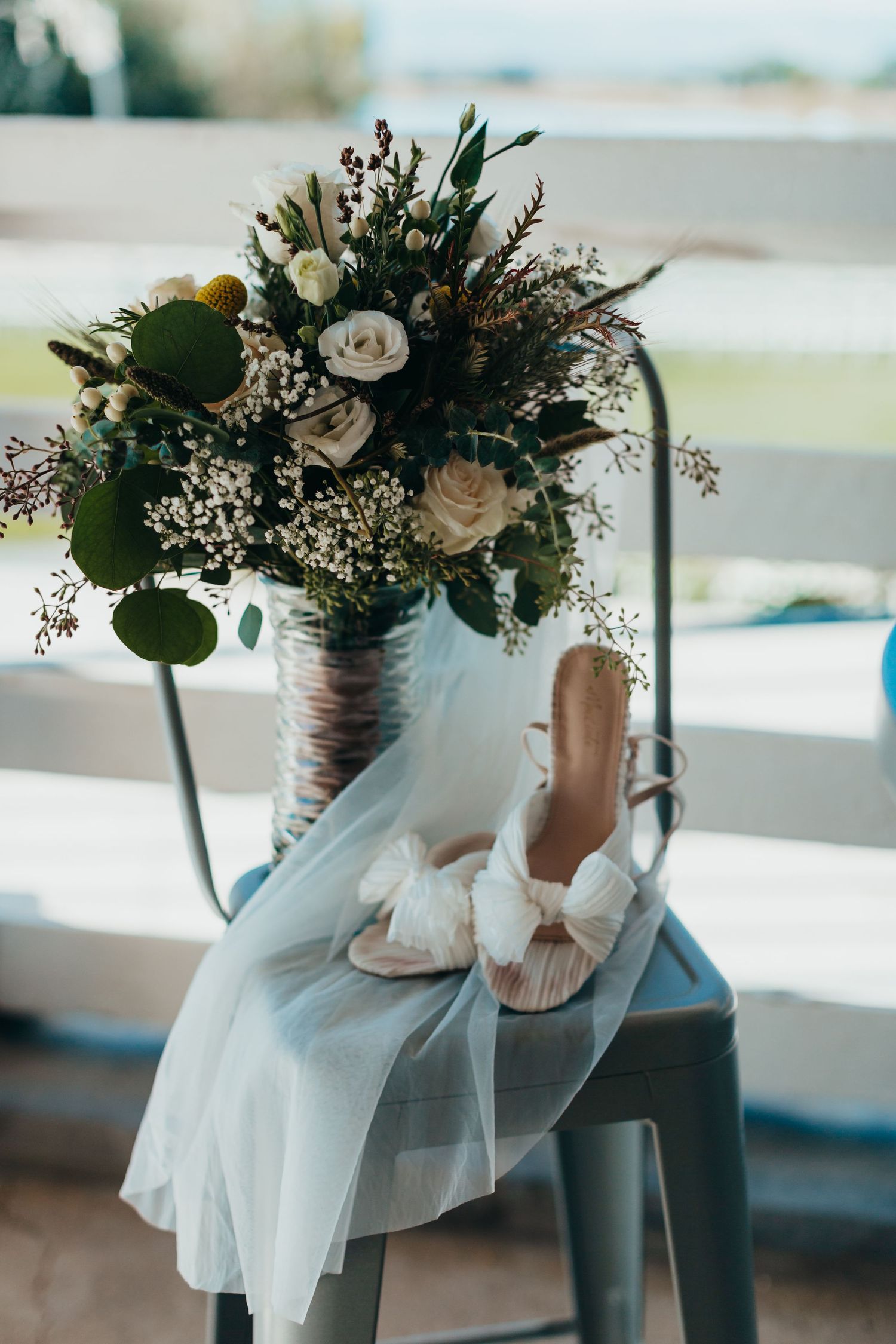 Wedding details featuring bridal bouquet with white roses and greenery alongside elegant bow shoes.
