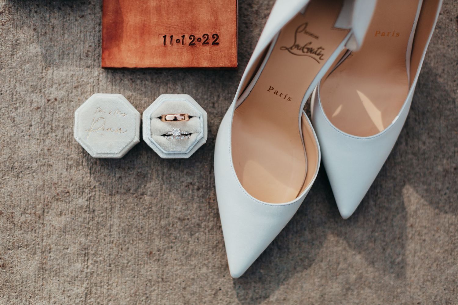 Pale blue pointed-toe bridal shoes with ring boxes on concrete surface.