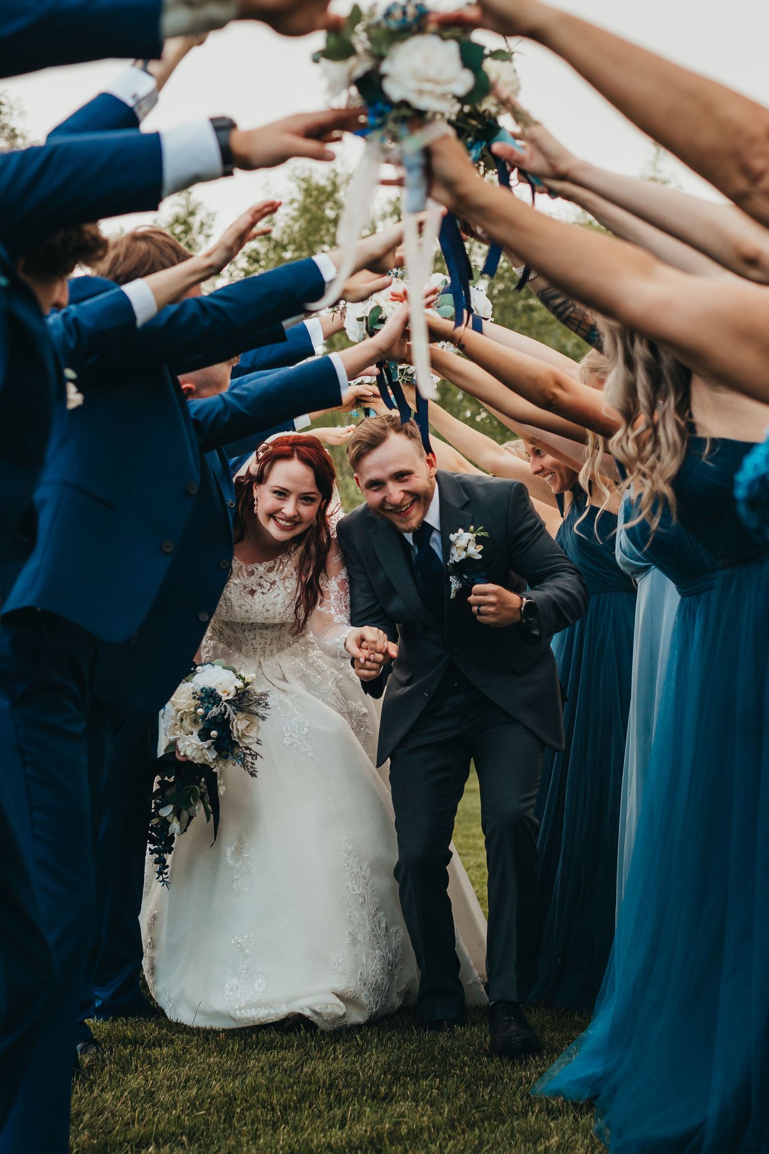 Wedding party creates an archway of arms for the newlyweds to pass through, with bridesmaids in blue dresses.