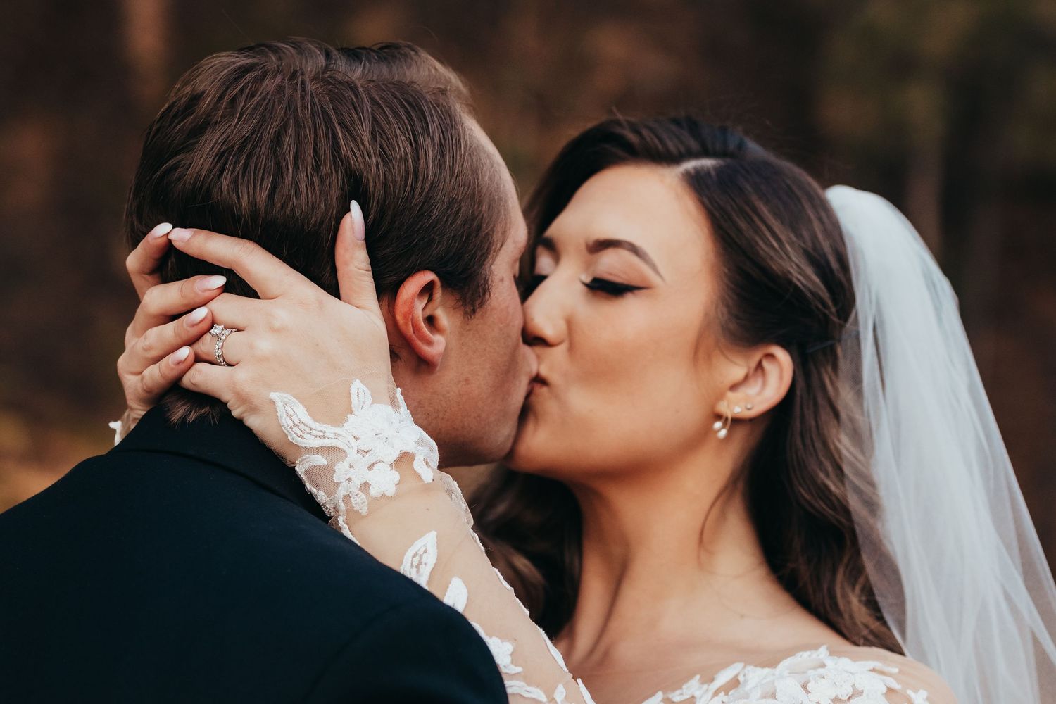 A romantic wedding kiss captured in an intimate outdoor setting with soft natural lighting.