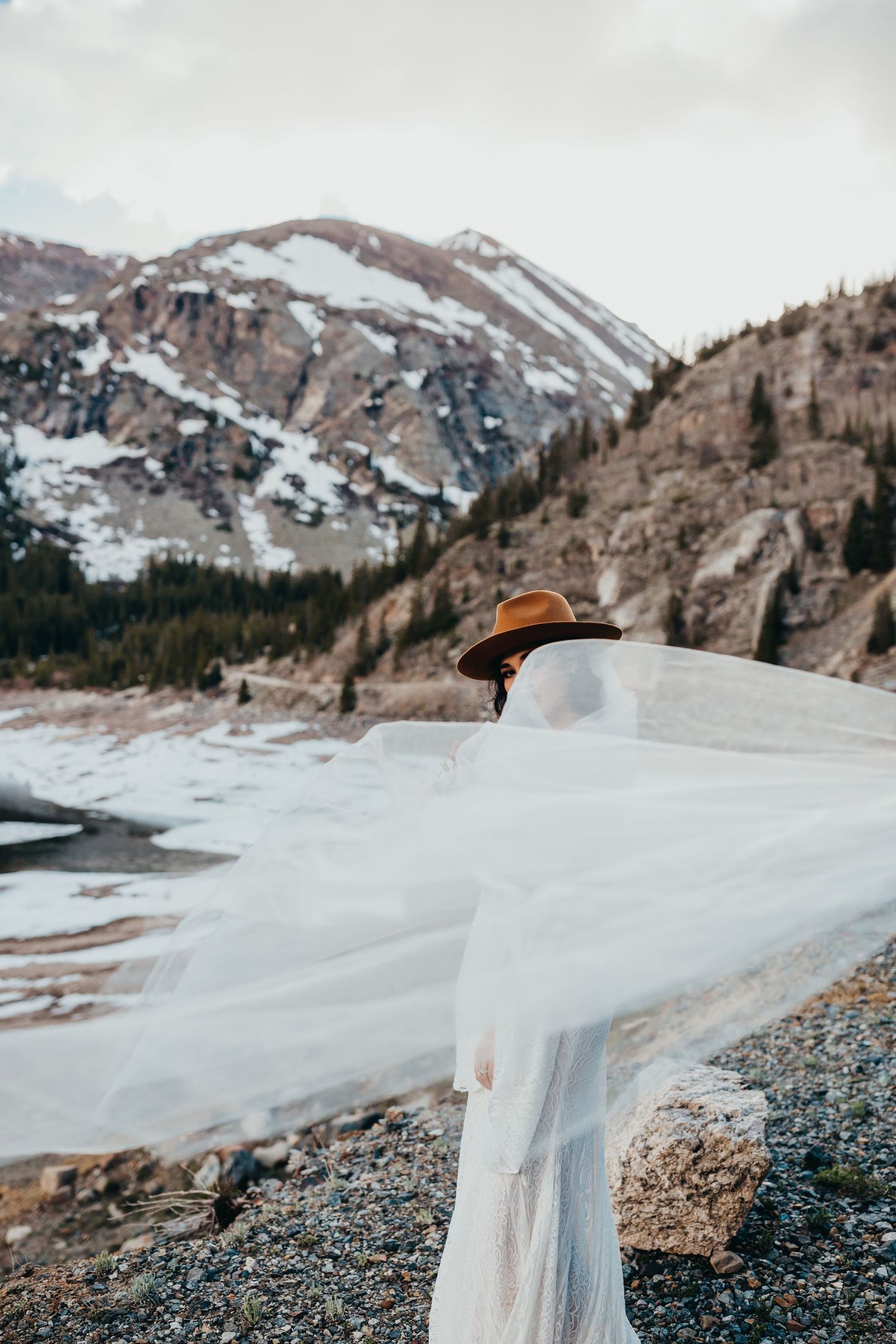 Flowing white wedding dress veil caught in the wind against snowy mountain backdrop.