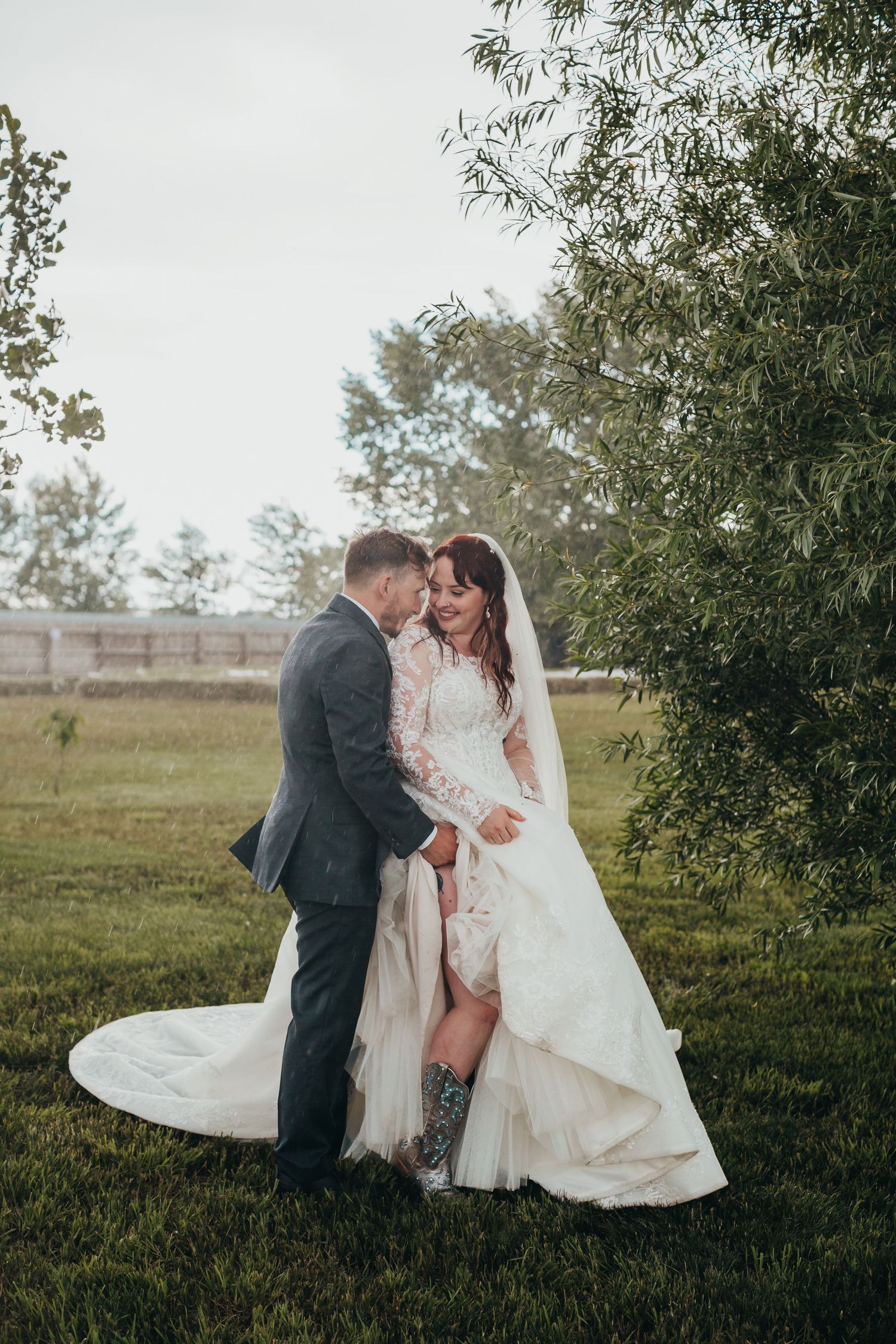 Playful wedding portrait showing off boots under elegant wedding dress in countryside setting.